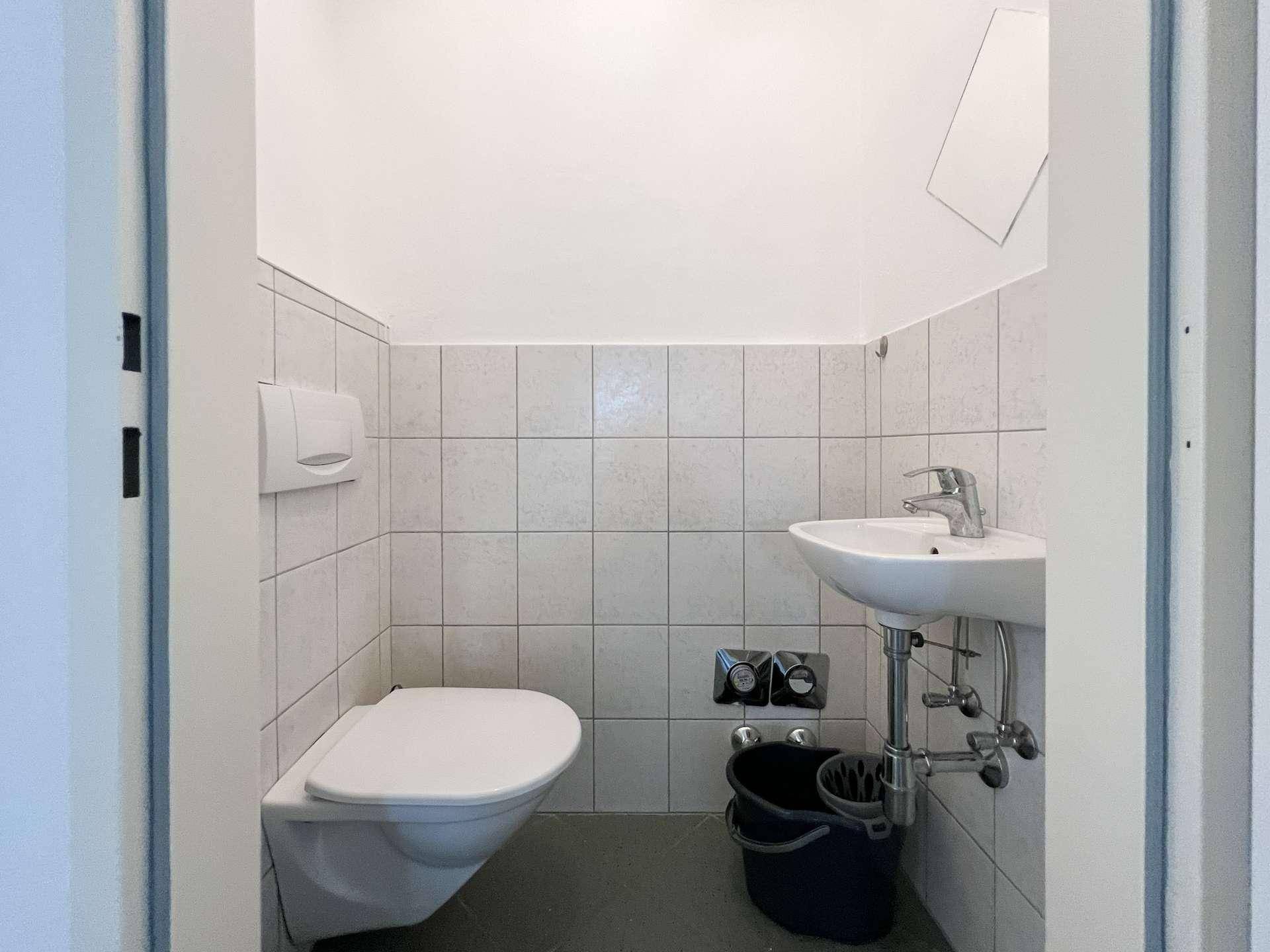 Separates WC mit wandhängender Toilette und kleinem Handwaschbecken.