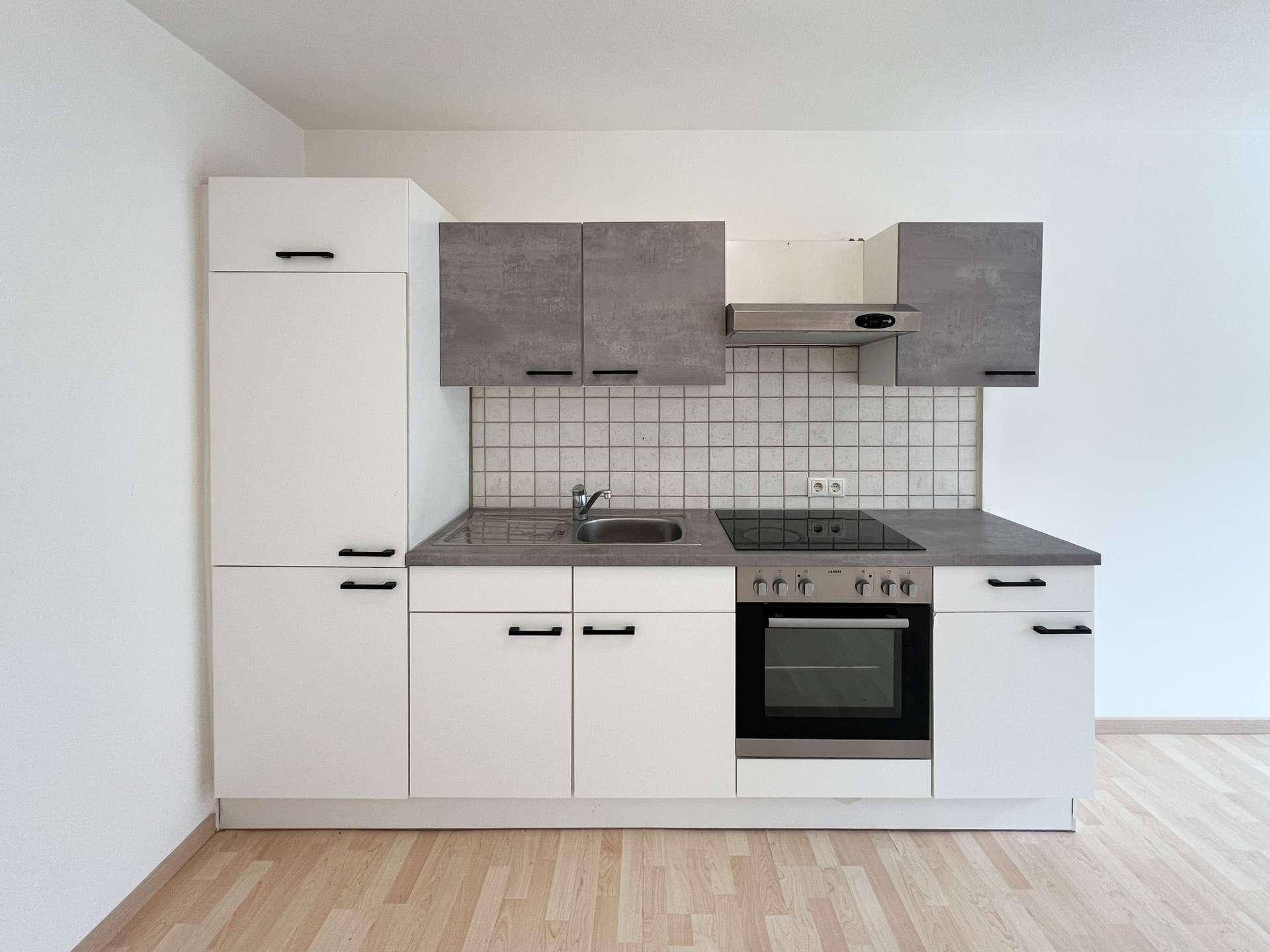 Moderne Küchenzeile mit weißen und grauen Schränken, Kochfeld und Backofen.