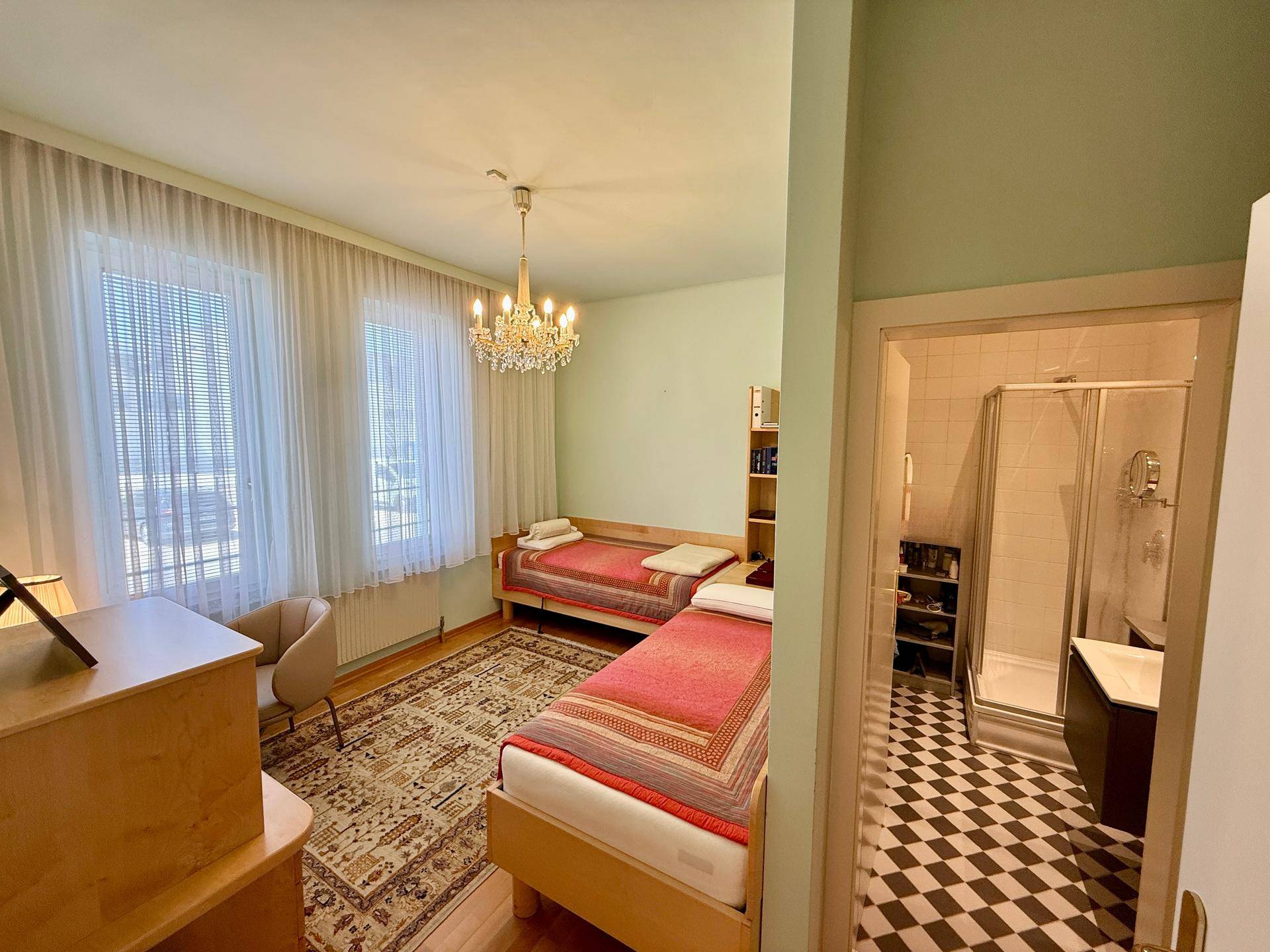 Helles Schlafzimmer mit zwei Einzelbetten und Zugang zu einem modernen Duschbad.