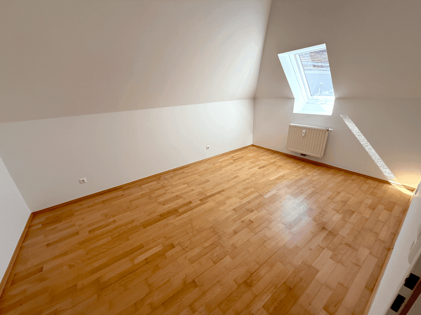 Helles Schlafzimmer im Dachgeschoss mit Holzboden, weiß gestrichenen Wänden und einem Dachfenster.
