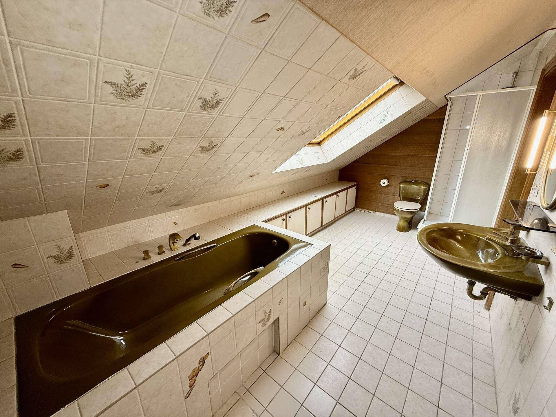 Dachgeschoss-Badezimmer mit Badewanne, Dachfenster und gemusterten Fliesen.