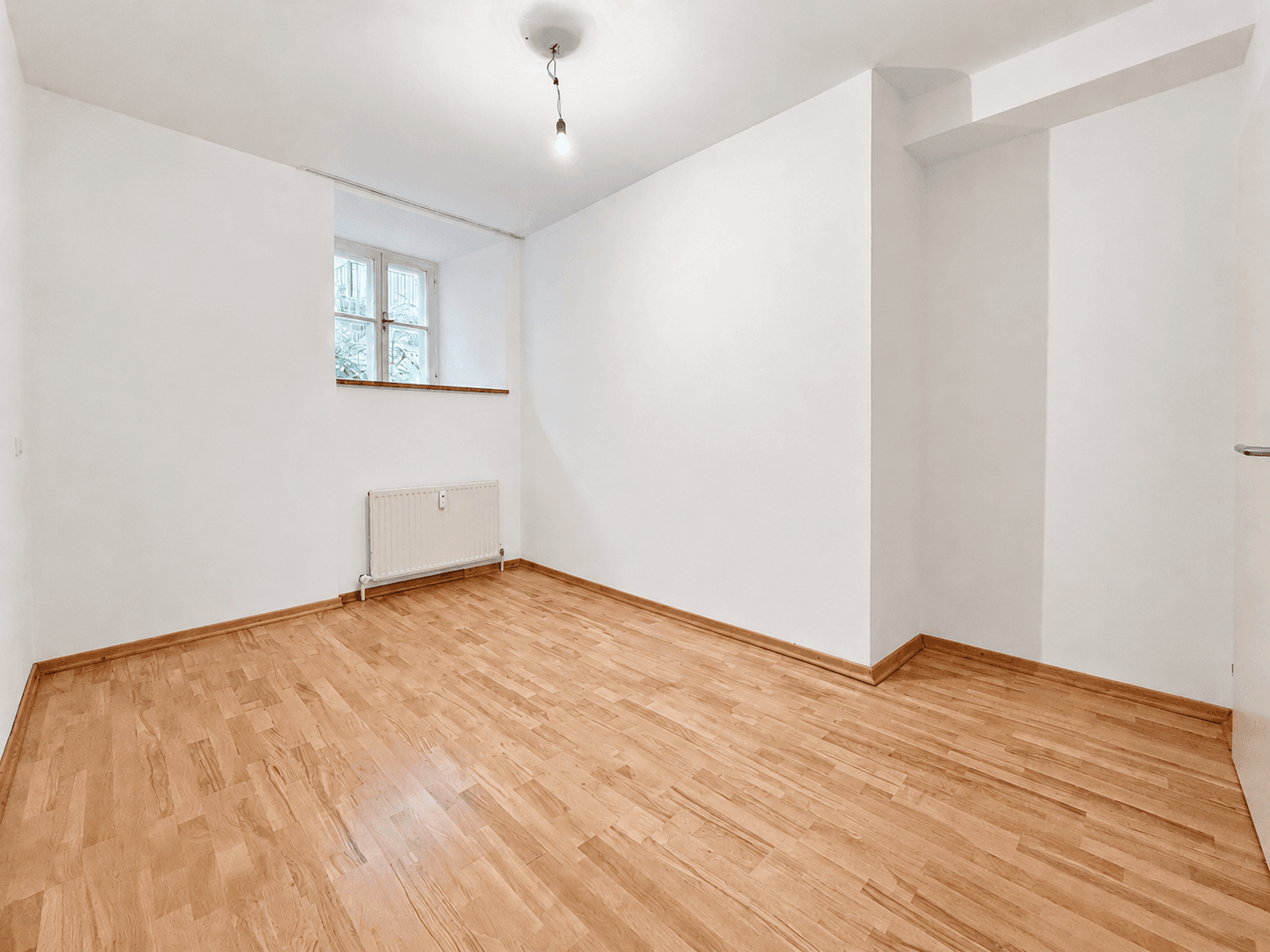 Helles Zimmer mit Holzboden und Fenster, bietet eine angenehme Atmosphäre.