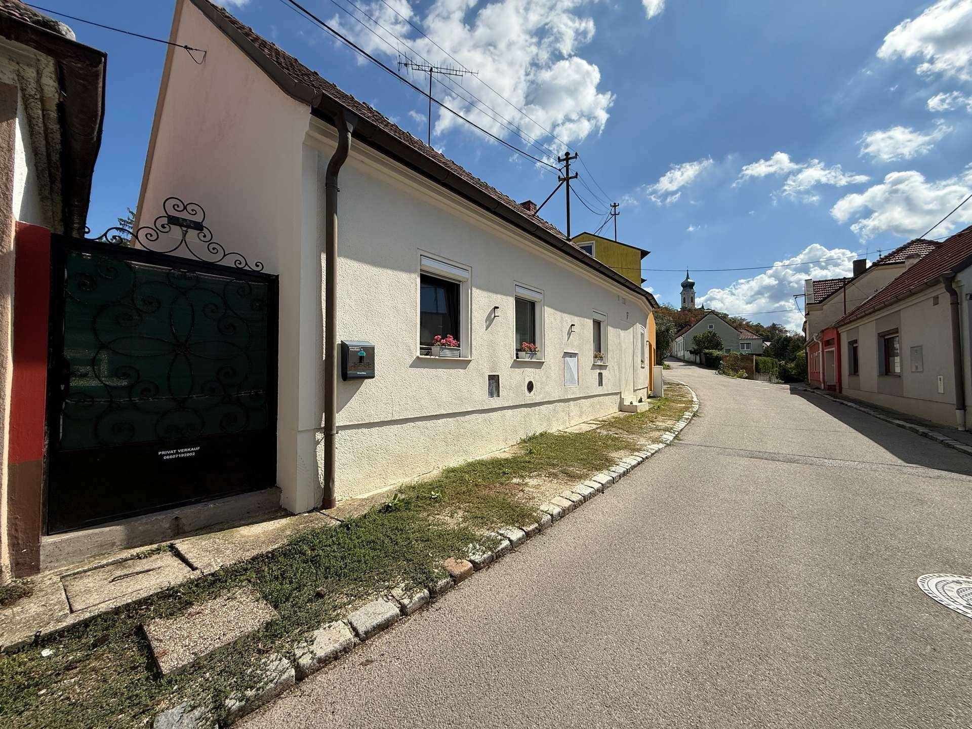 Traditionelles Haus mit weißer Fassade, schmiedeeisernem Tor und Blick auf die Straße.