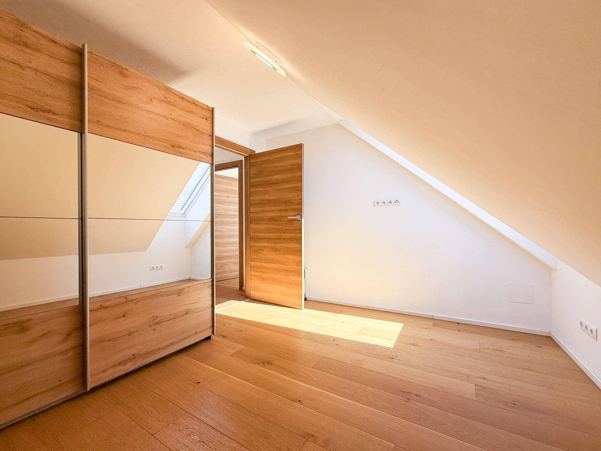 Schlafzimmer mit großem Spiegelschrank, Holzboden und einem Dachfenster, das durch die offene Tür sichtbar ist.