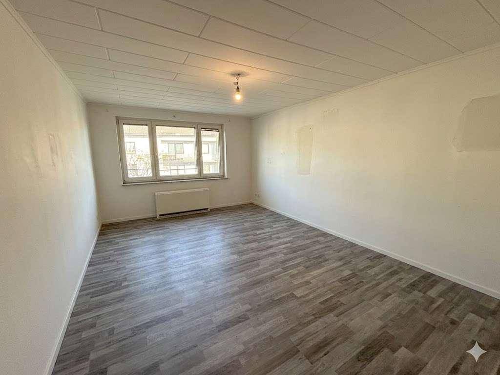 Geräumiges, leeres Zimmer mit Laminatboden und einem Fenster, das Tageslicht hereinlässt.