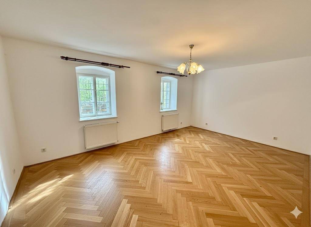 Helles, leeres Zimmer mit Fischgrätparkett und großen Fenstern, ideal für Wohn- oder Schlafbereich.