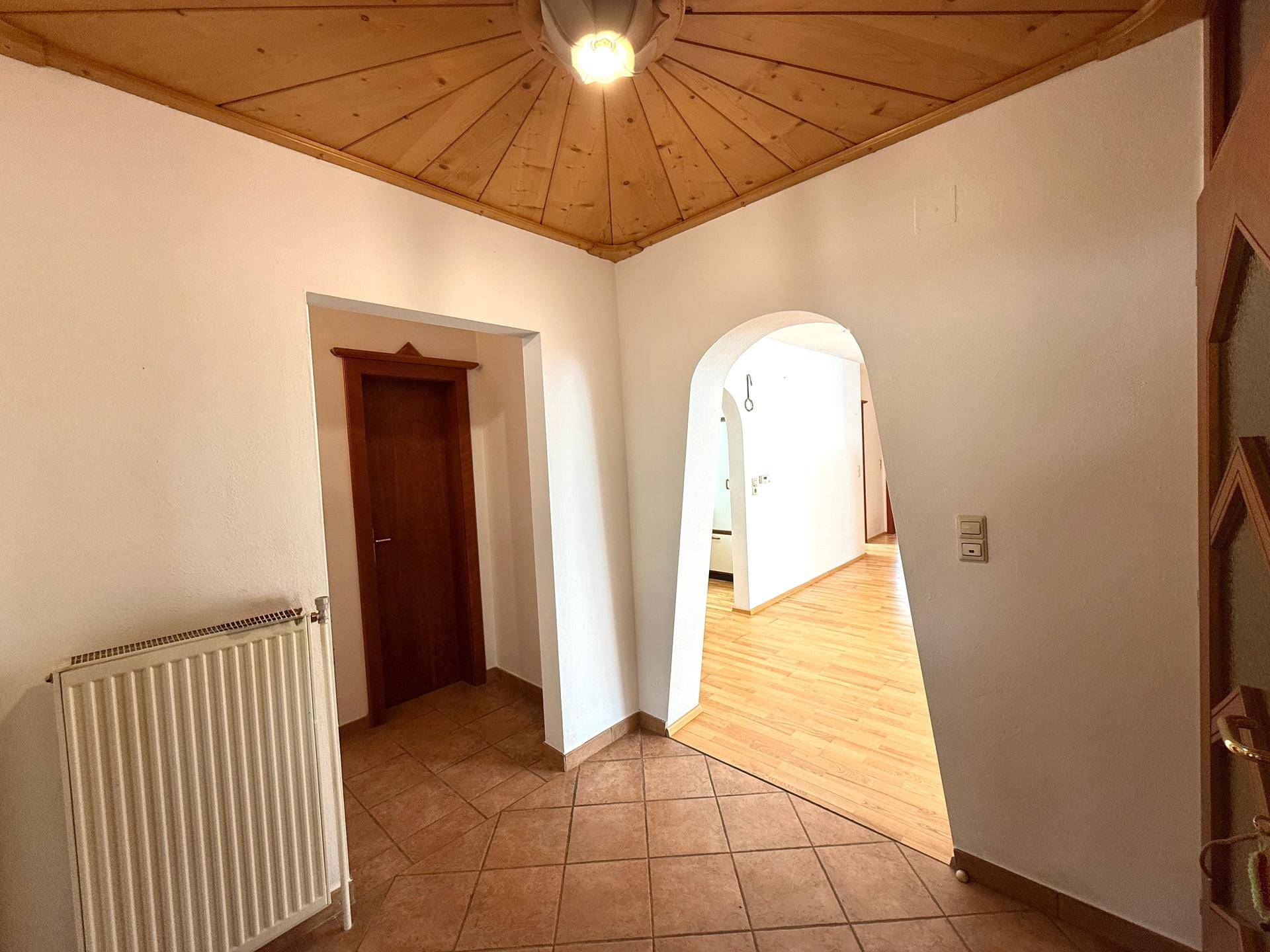 Einladender Eingangsbereich mit Terrakotta-Fliesenboden, Holzdecke und einem dekorativen Rundbogen.