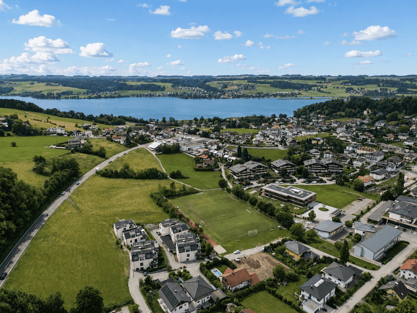 Weitläufige Luftaufnahme einer Stadt am See, umgeben von grünen Hügeln.