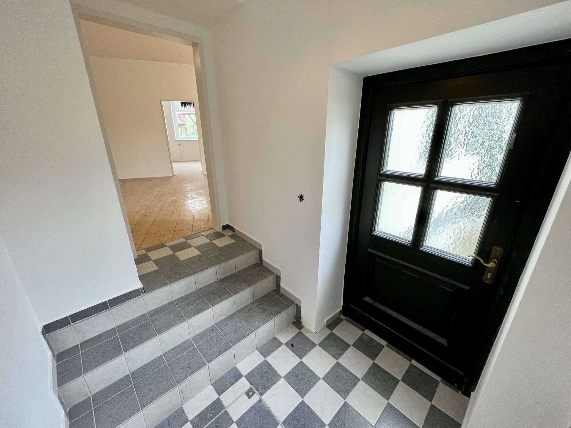 Eingangsbereich mit schwarz-weiß karierten Fliesen und einer dunklen Eingangstür mit Glaseinsätzen.
