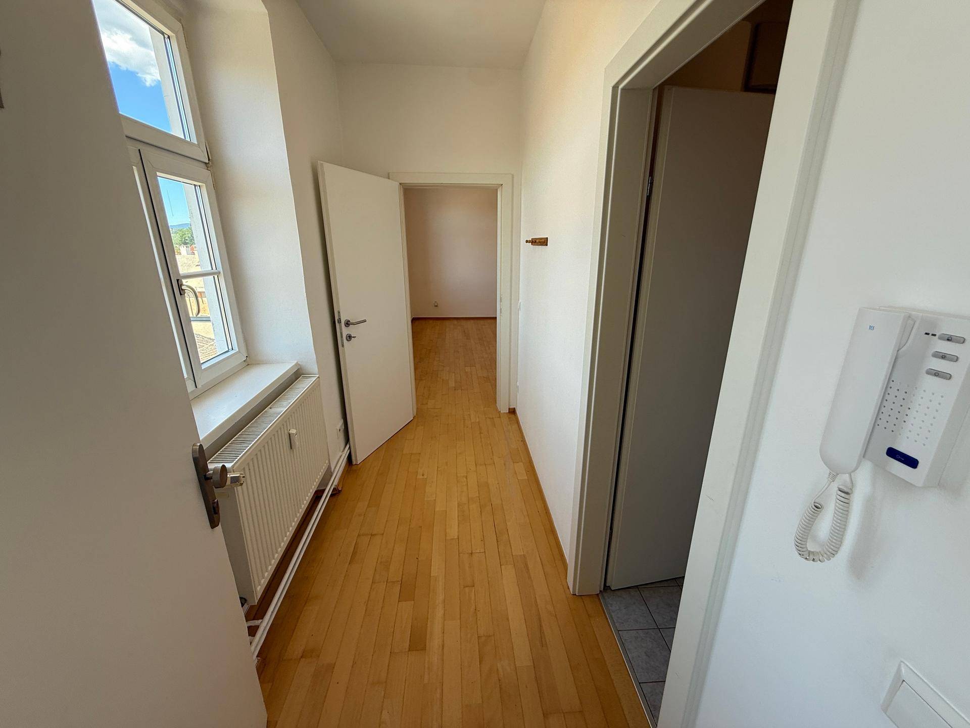 Langer Flur mit Holzboden, Fenstern und Zugang zu verschiedenen Zimmern der Wohnung.