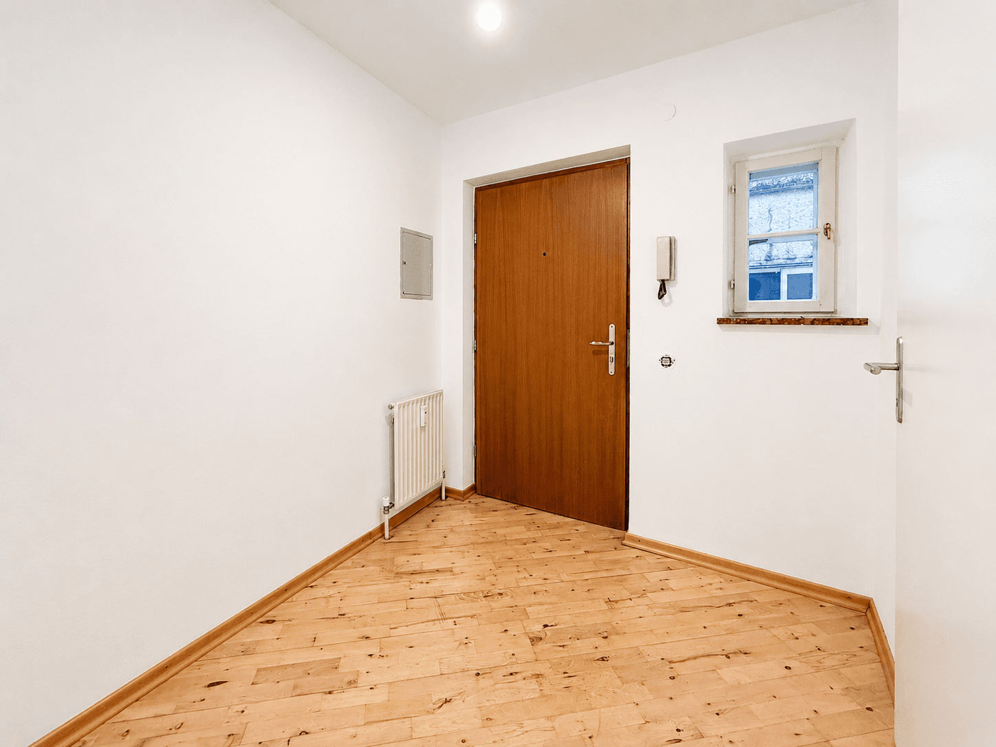 Eingangsbereich mit Holzboden, weiß gestrichenen Wänden und Haustür.
