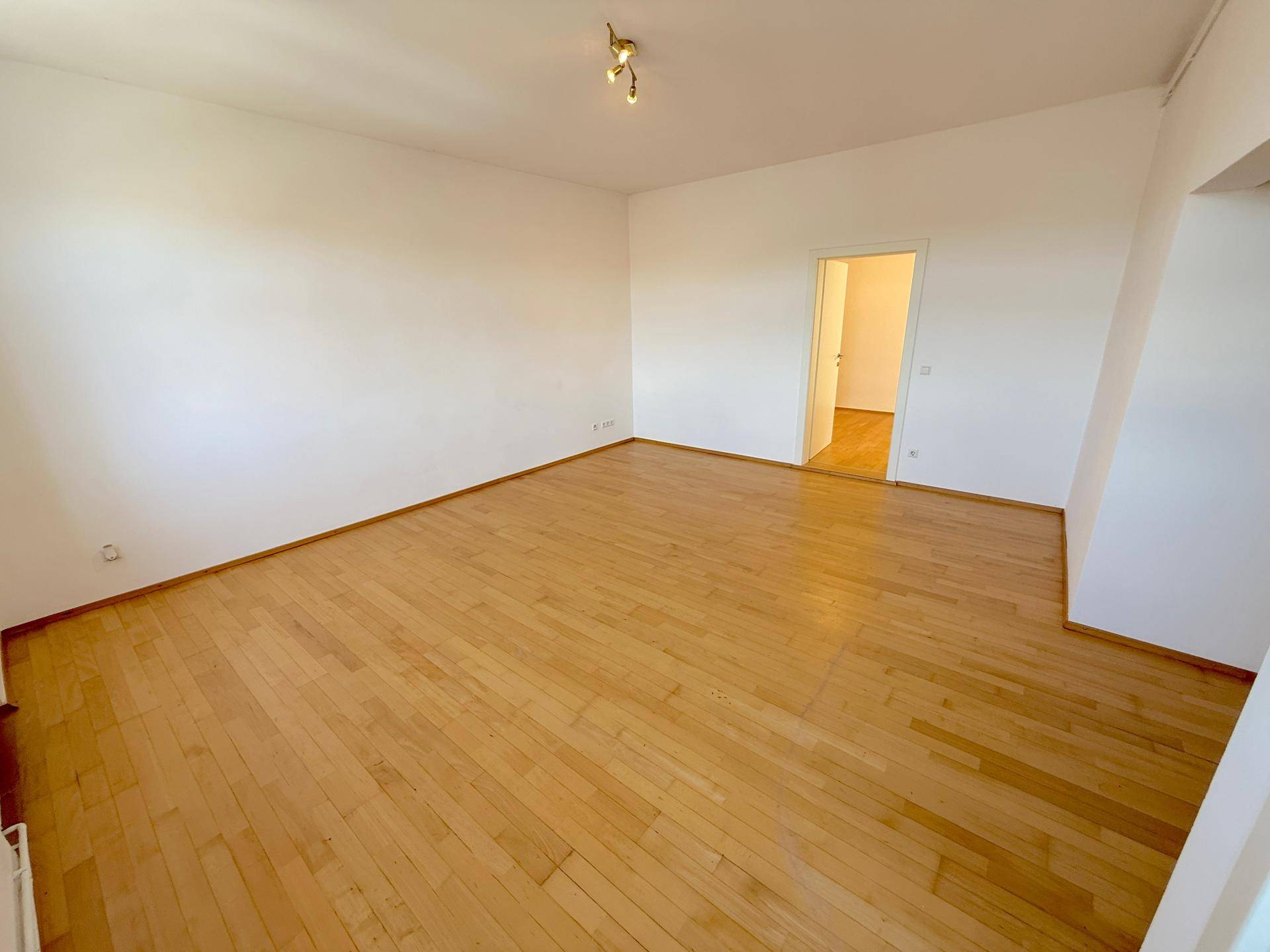 Geräumiges, helles Zimmer mit Holzboden und weiß gestrichenen Wänden, bereit zur Einrichtung.