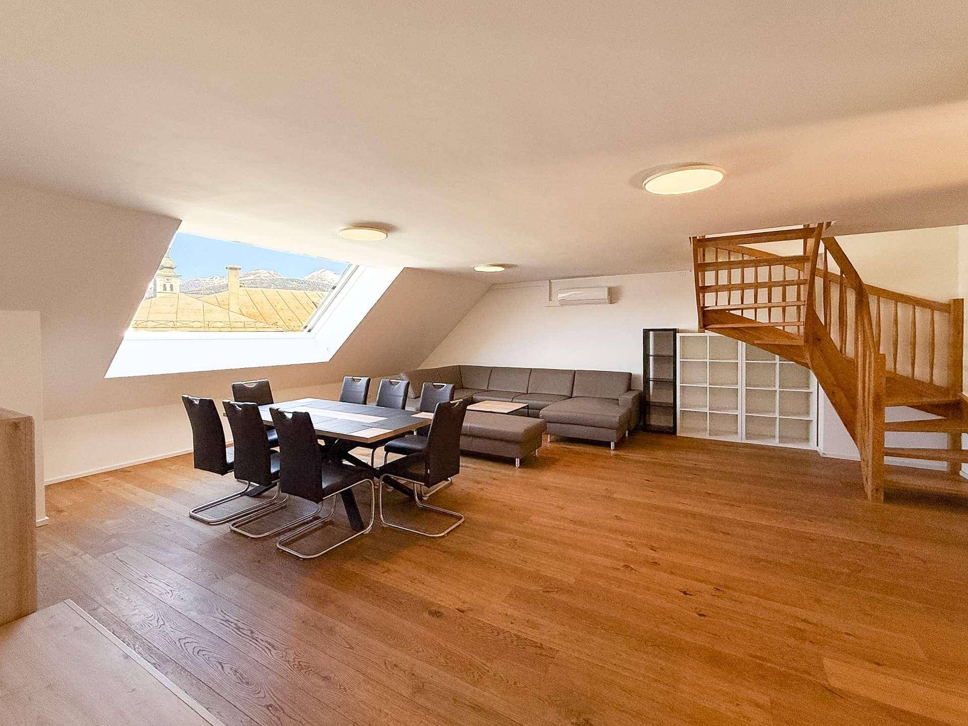 Heller und offener Wohn-Essbereich mit Holzboden, Dachfenster und einer markanten Holztreppe.