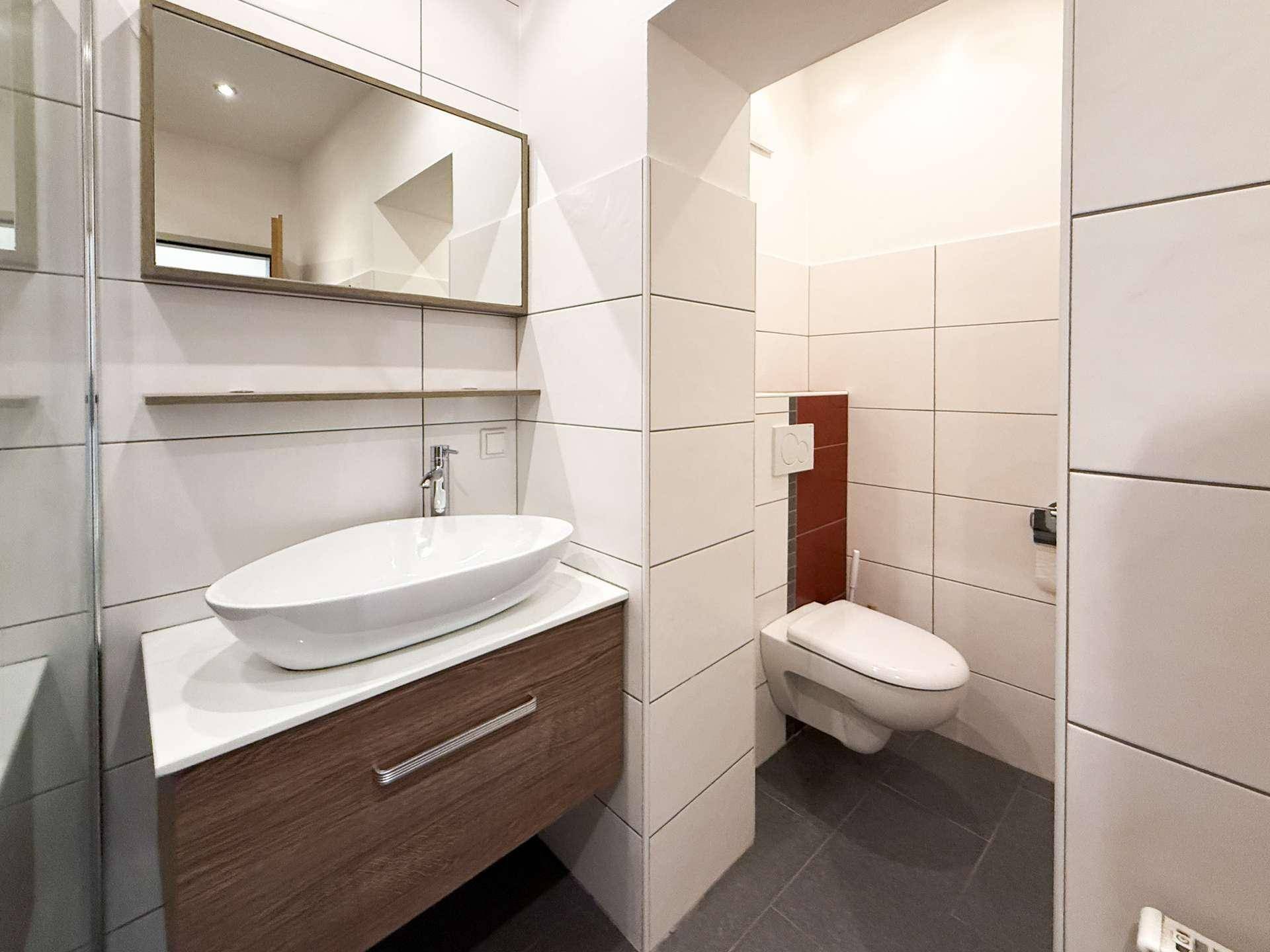 Modernes Badezimmer mit Waschbecken, Spiegel und separatem WC-Bereich.