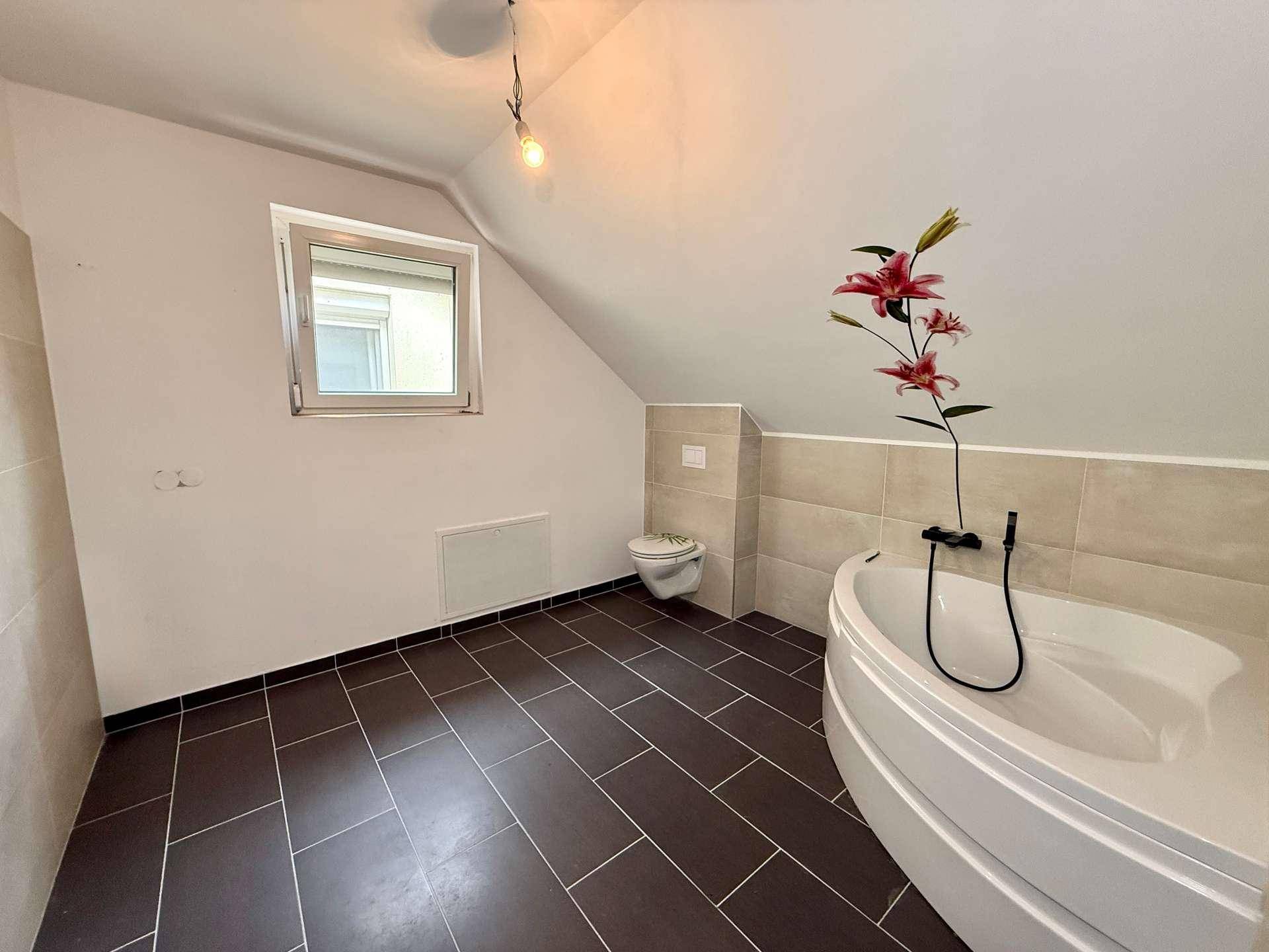 Badezimmer im Dachgeschoss mit Eckbadewanne, Toilette und Fenster.