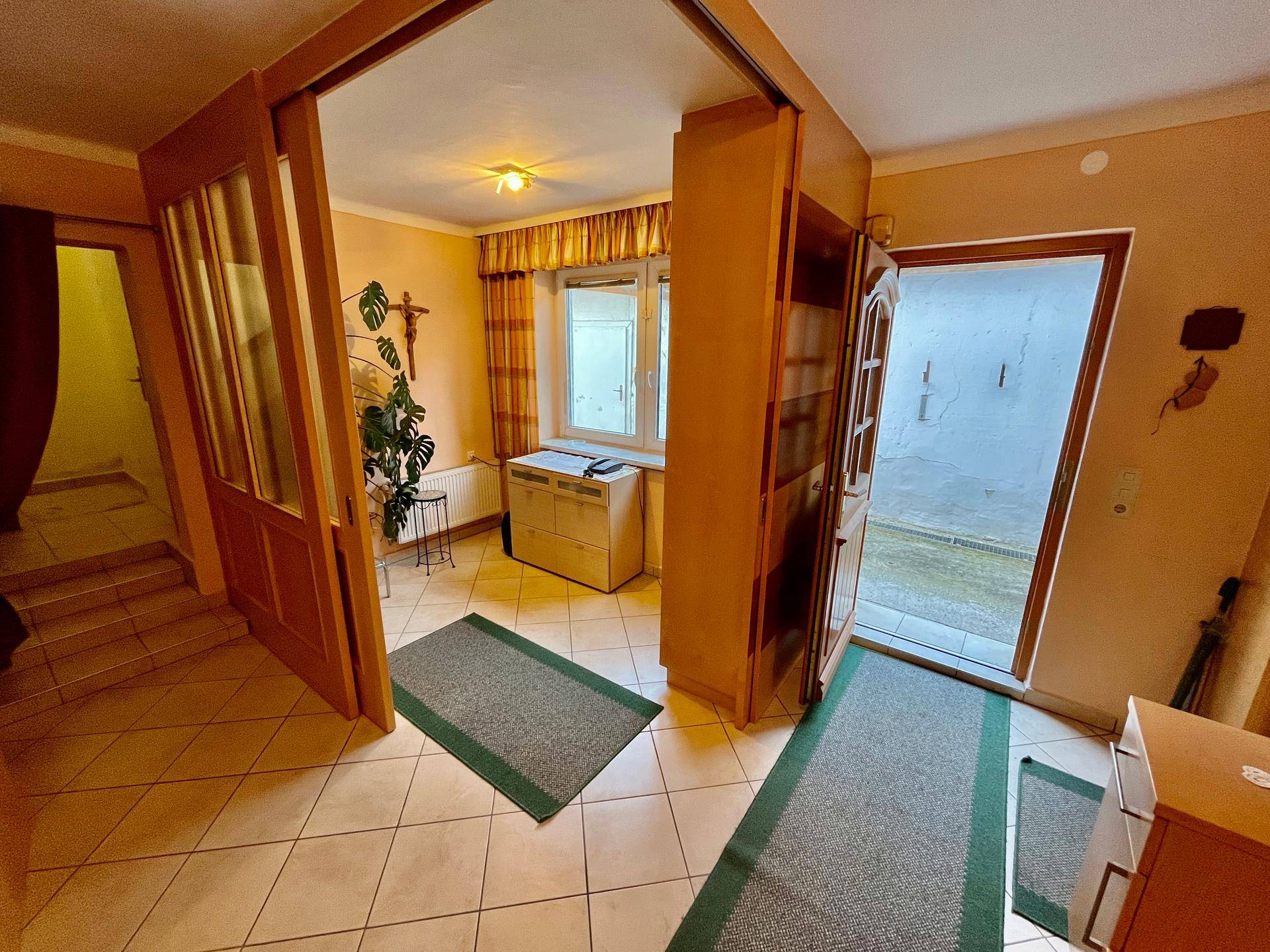 Heller Eingangsbereich mit Fliesenboden, Fenster und Zugang zu weiteren Räumen.