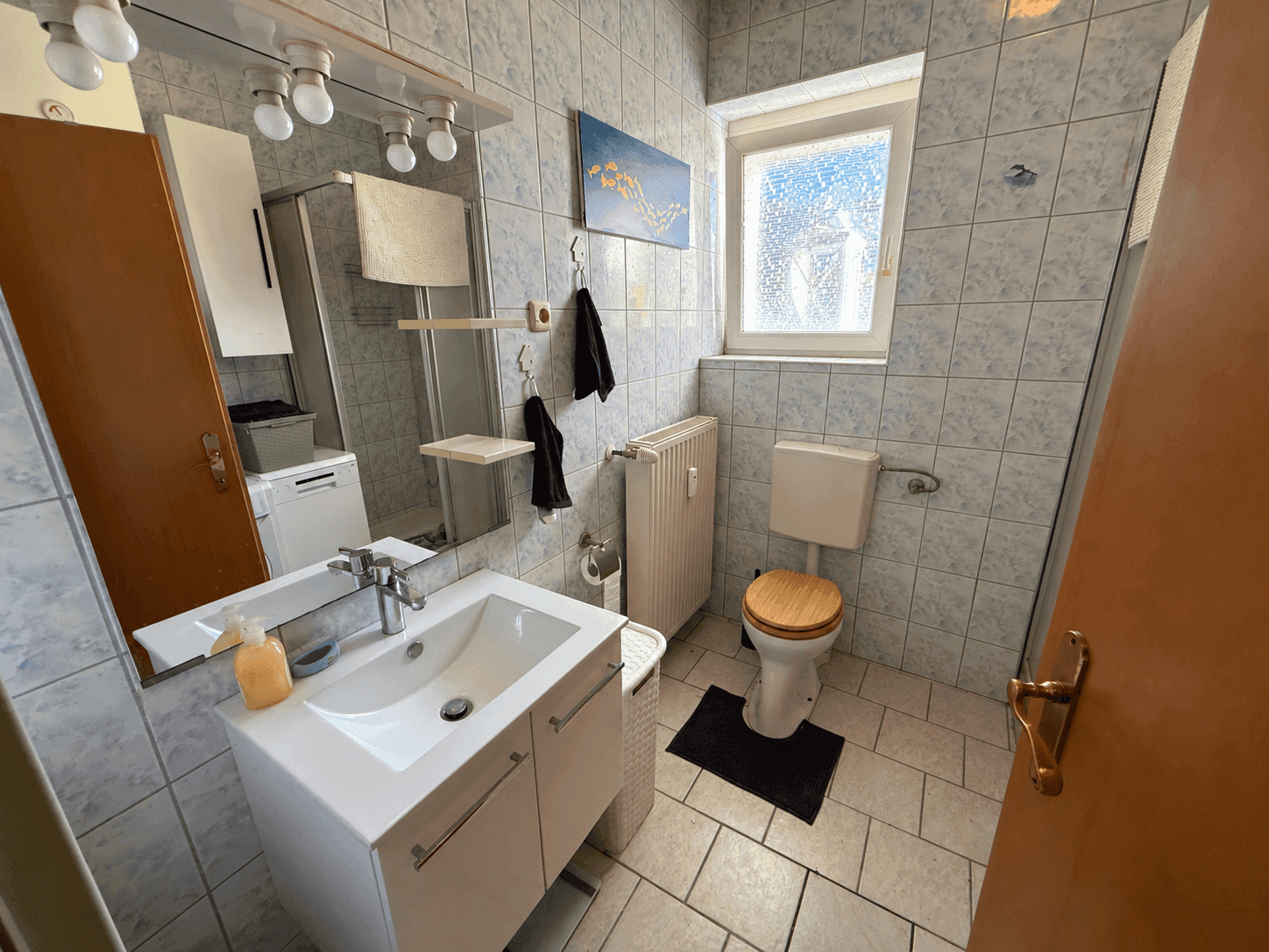 Badezimmer mit hellblauen Fliesen, Dusche, WC und Fenster für Tageslicht.