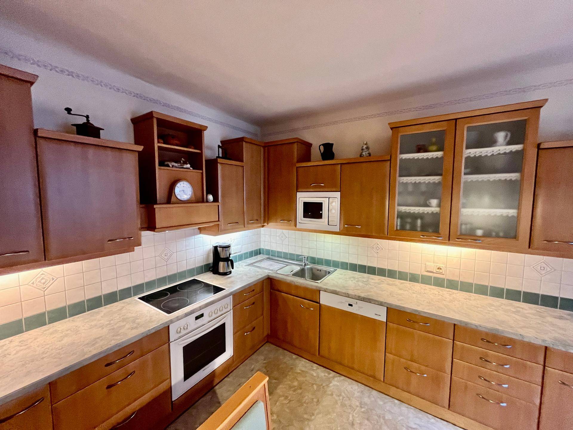 Funktionale Küche mit Holzschränken, integrierten Geräten und heller Arbeitsplatte.