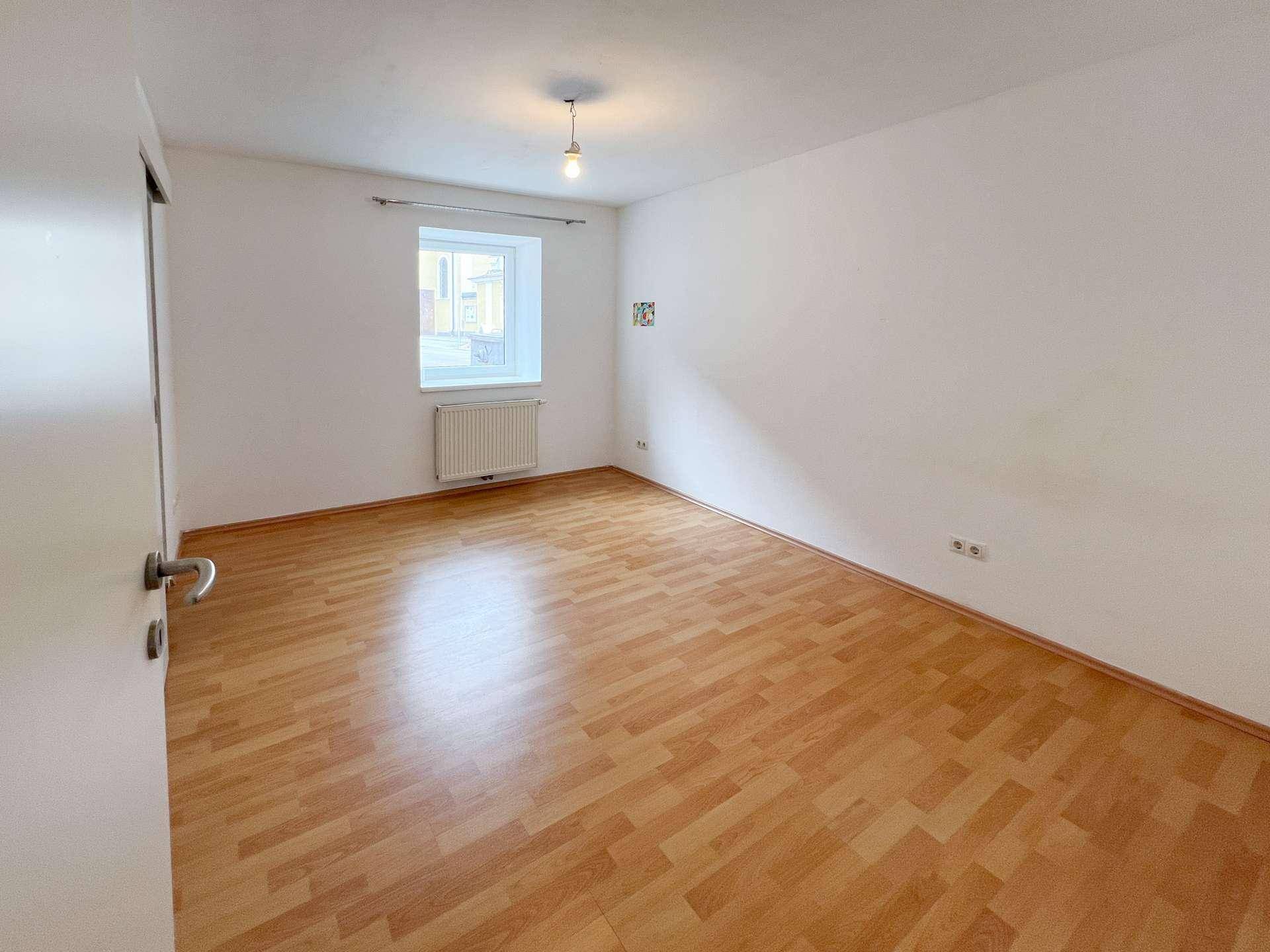 Helles Schlafzimmer mit Laminatboden und einem Fenster mit Blick nach draußen.