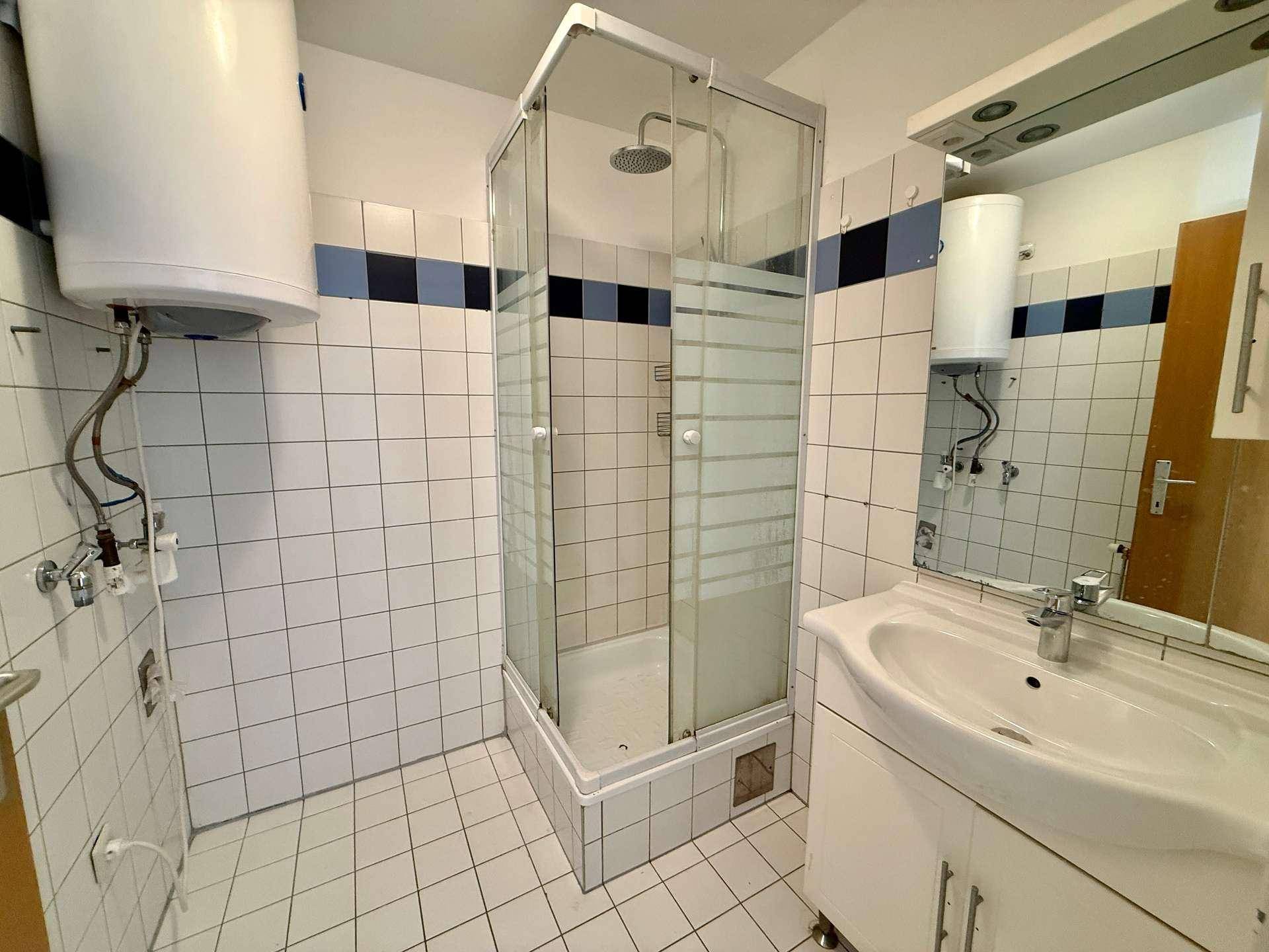 Badezimmer mit Duschkabine, Waschbecken und Boiler, ausgestattet mit weißen Fliesen.
