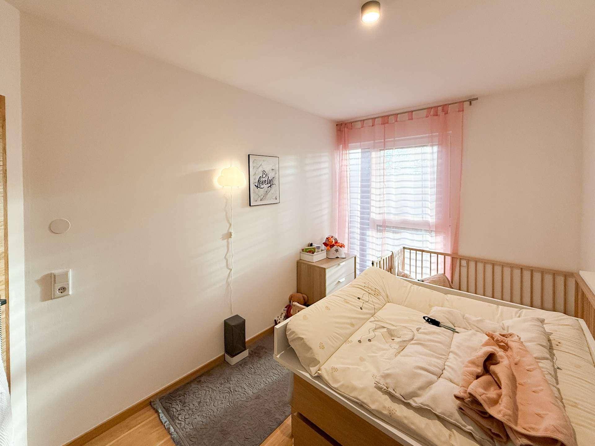 Helles Kinderzimmer mit Babybett, Wickeltisch und Fenster mit rosa Vorhängen.