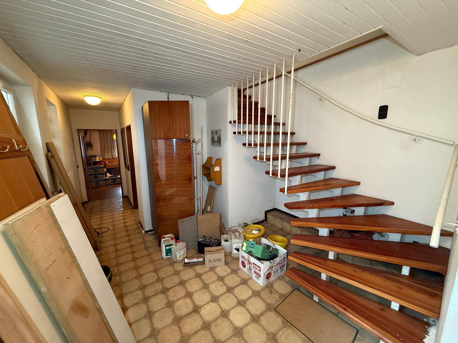 Flur mit Holztreppe und Fliesenboden, der zu den oberen Etagen führt.