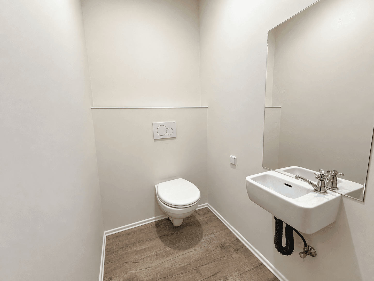 Kleines Gäste-WC mit wandhängendem WC, Waschbecken und Spiegel.