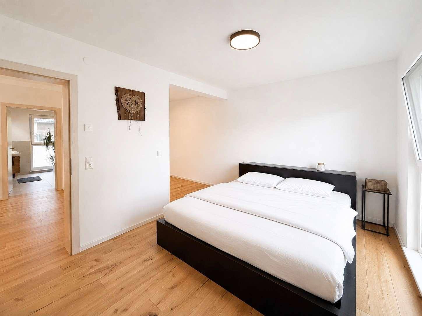 Schlafzimmer mit Holzboden, modernem Bett und Zugang zu einem weiteren Raum.