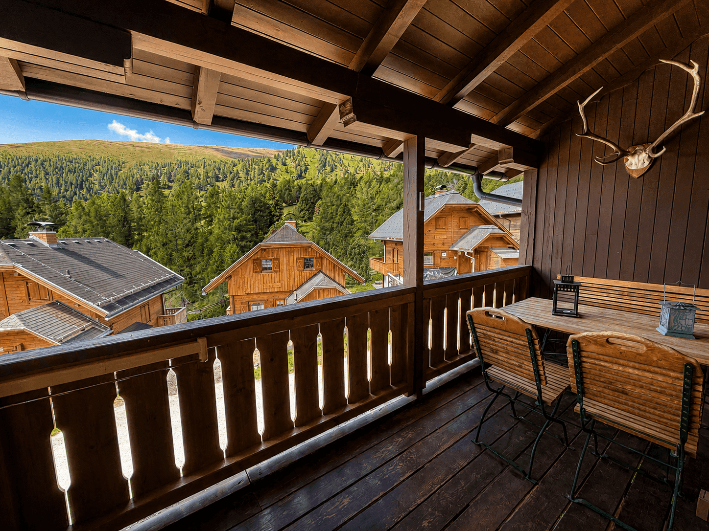 Geräumiger Holzbalkon mit Esstisch, Stühlen und weitem Blick auf die Berge.