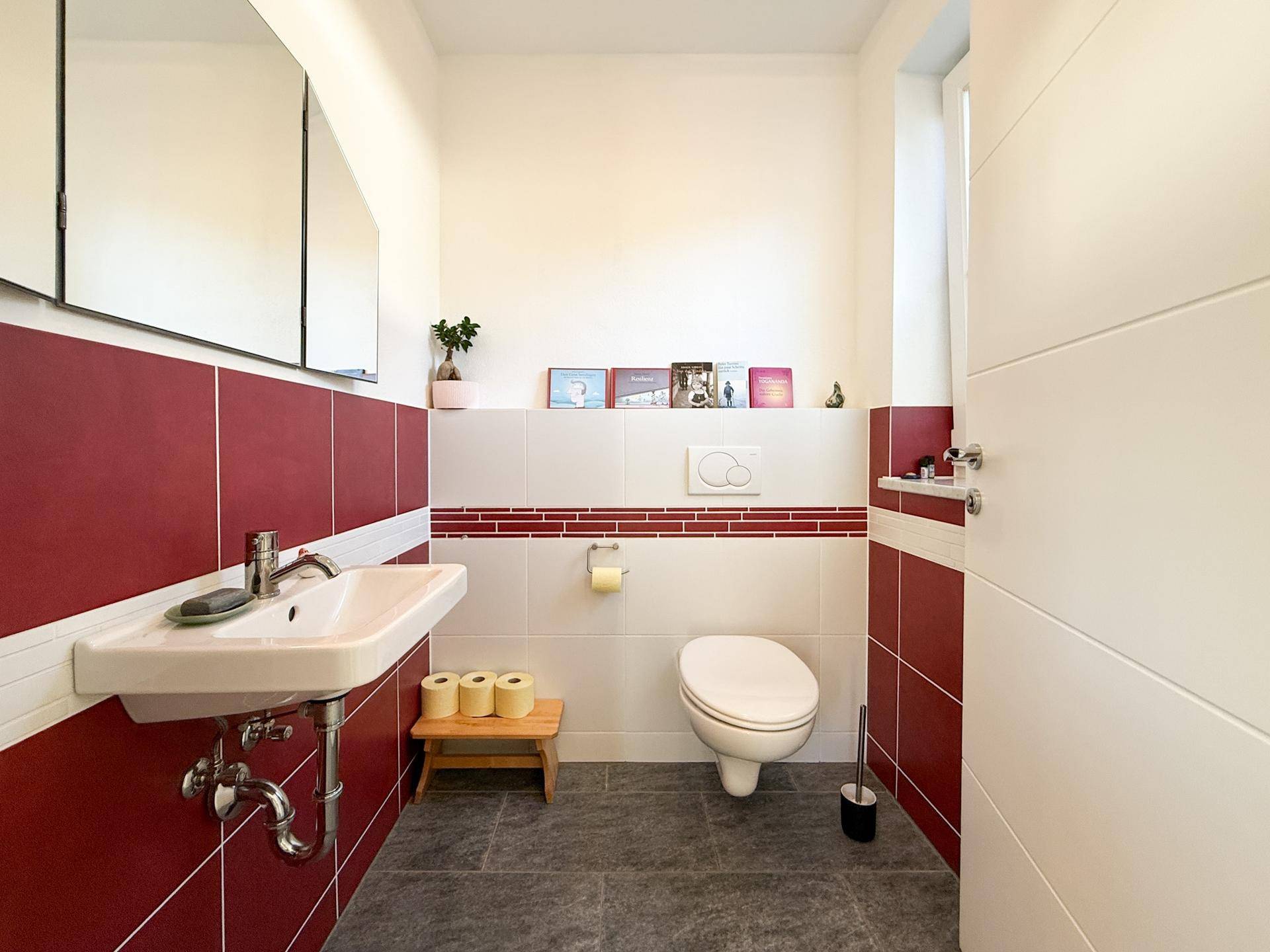 Modernes Gäste-WC mit roten und weißen Fliesen, Wand-WC und Einzelwaschbecken.