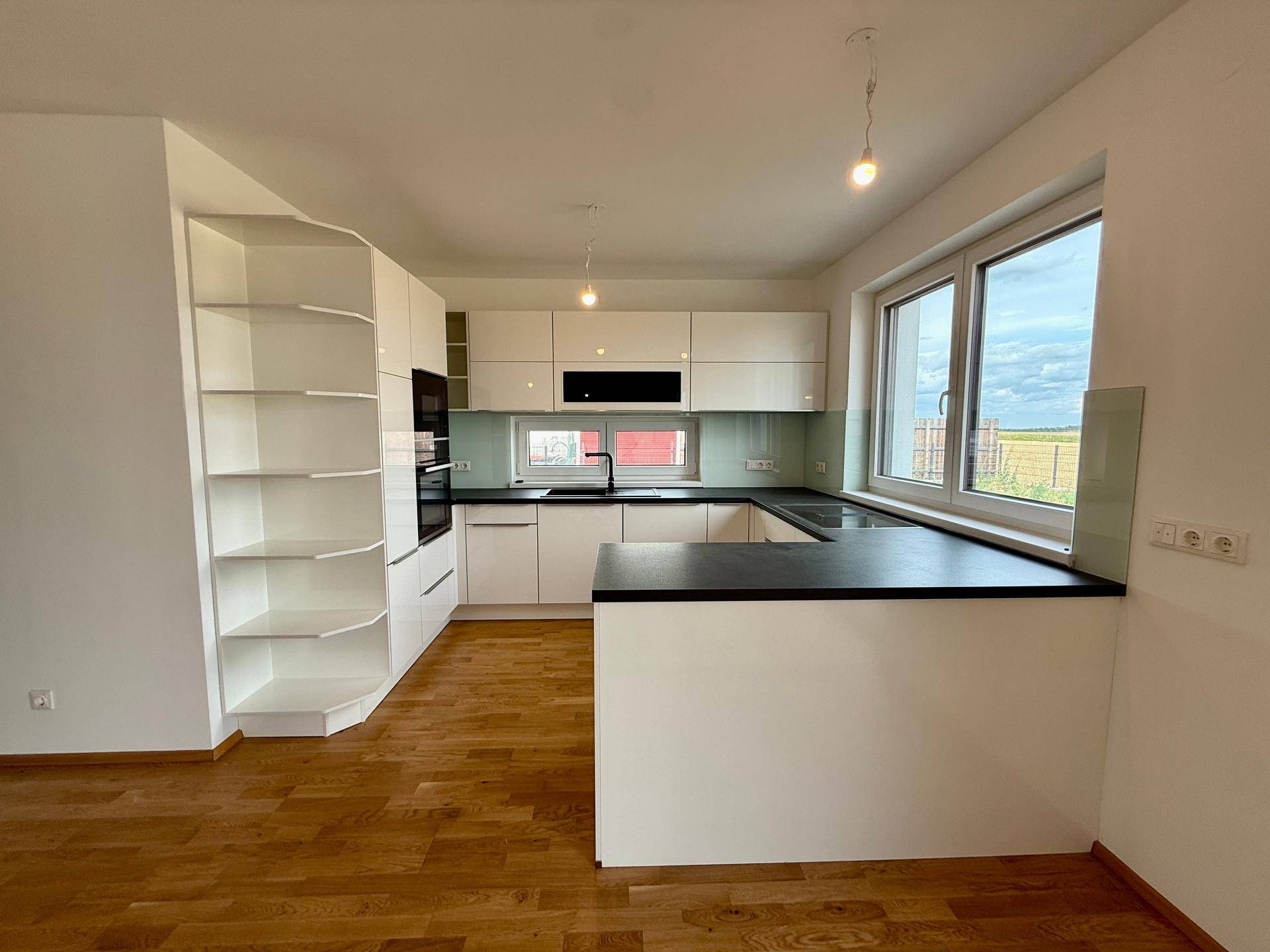 Moderne Einbauküche mit weißen Schränken, dunkler Arbeitsplatte und Fenster mit Blick ins Grüne.