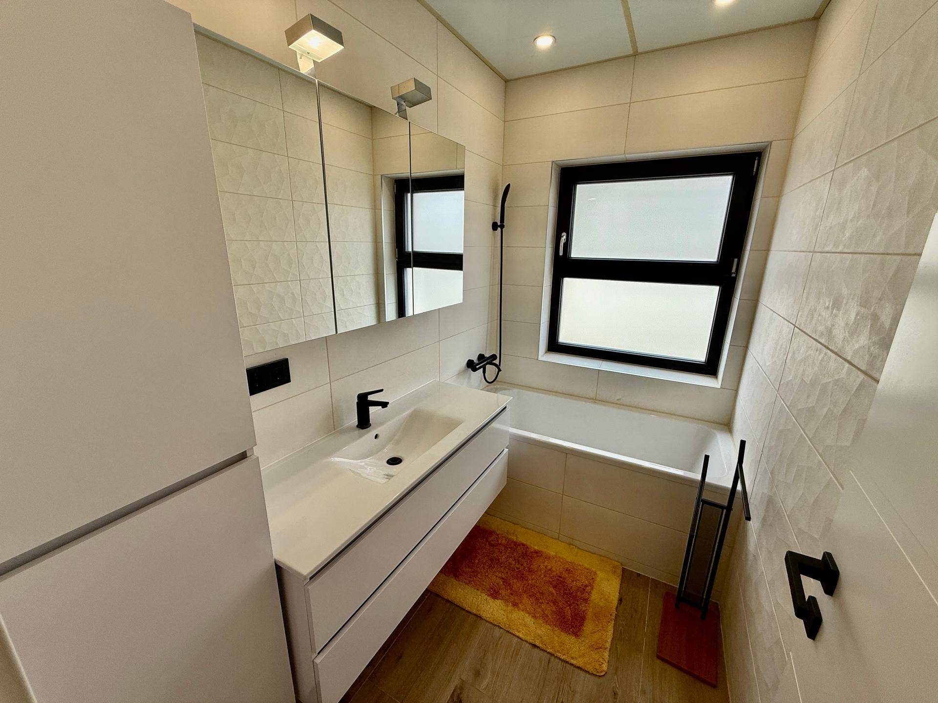 Modernes Badezimmer mit Badewanne, Einzelwaschbecken und einem Fenster für Tageslicht.
