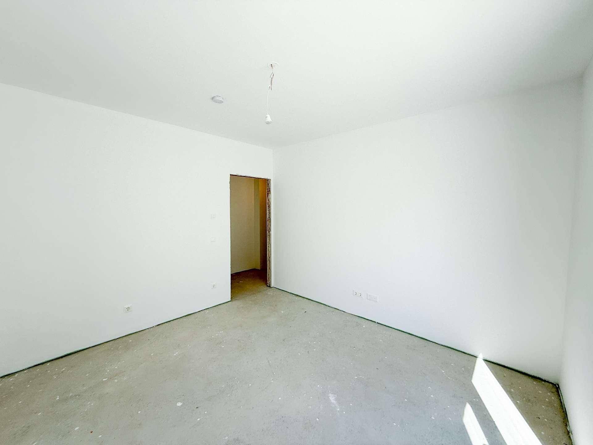 Leerer Rohbauraum mit Betonboden und weiß gestrichenen Wänden, bereit für die Innengestaltung.