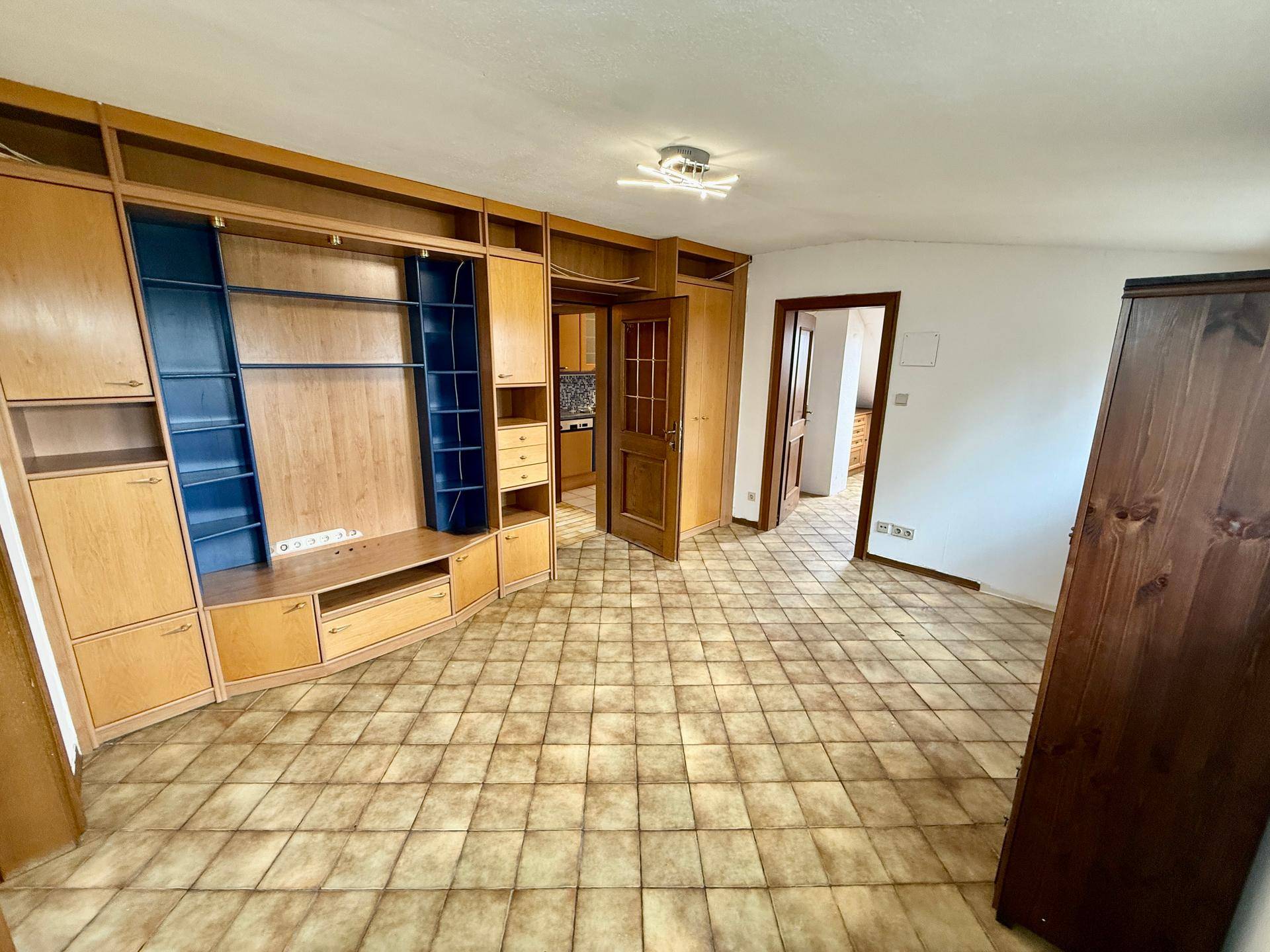 Geräumiges Dachgeschosszimmer mit großer Schrankwand und Fliesenboden.