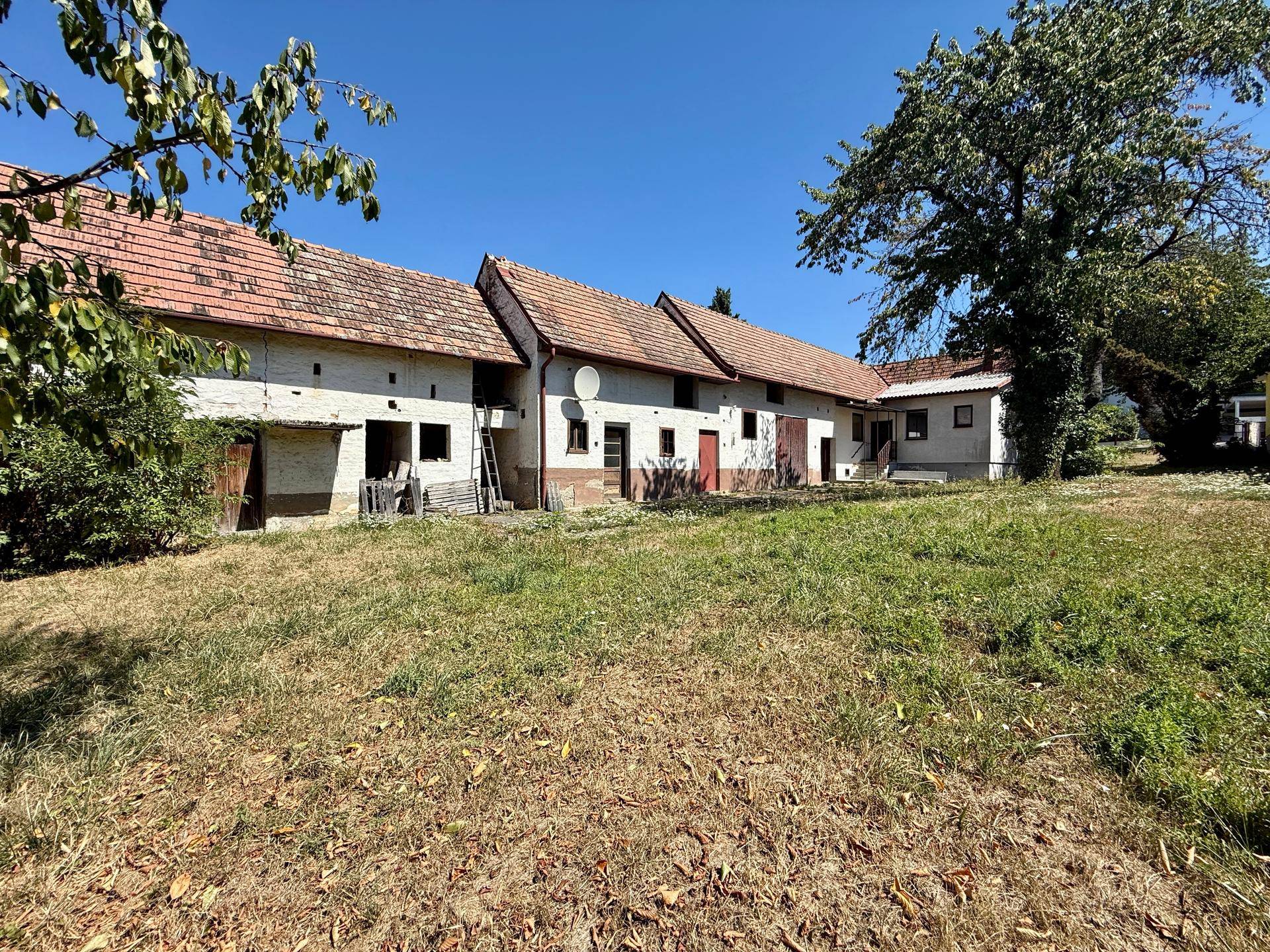 Ländliches Anwesen mit mehreren Gebäuden und großem Gartenbereich unter strahlendem Himmel.