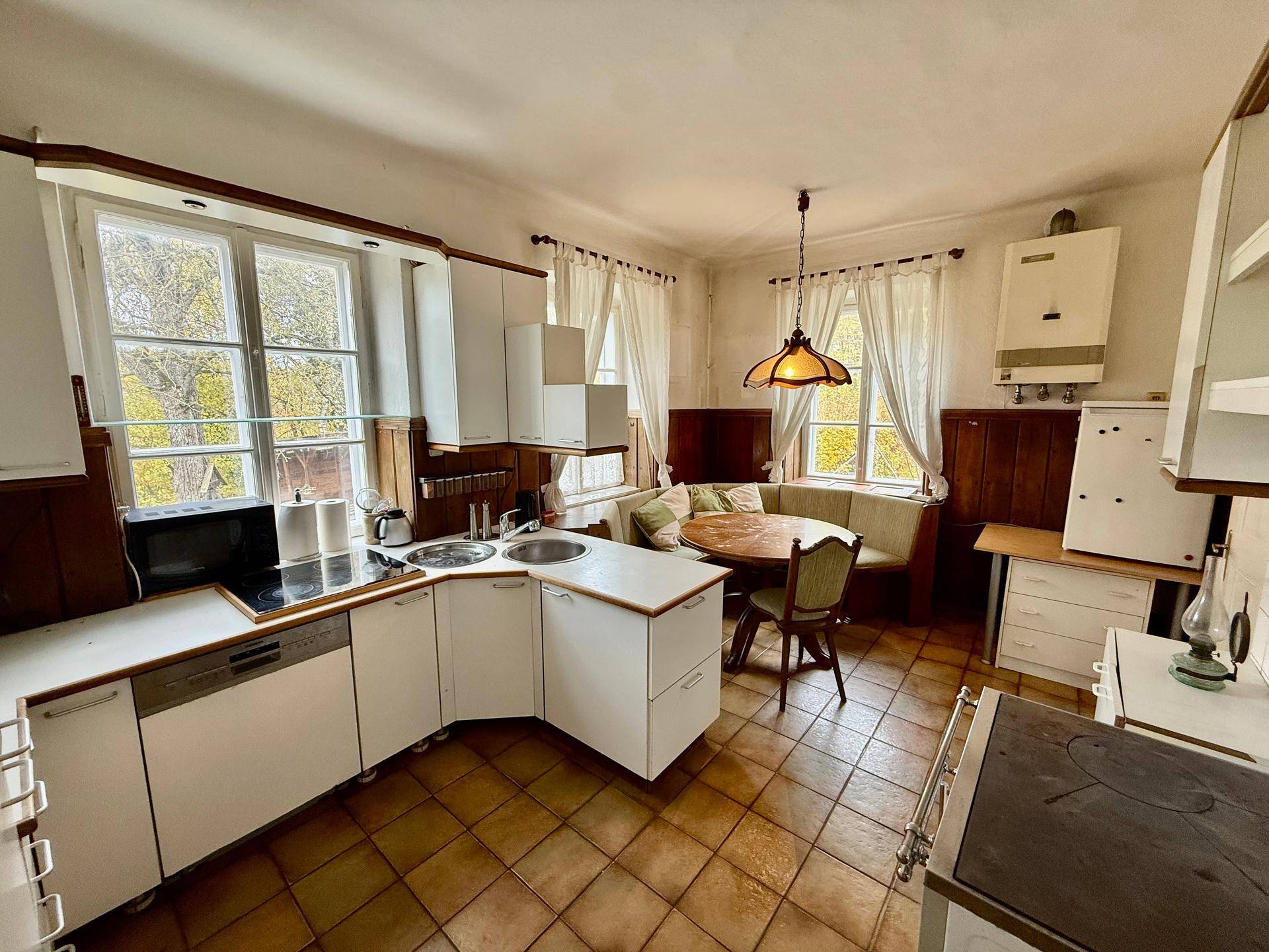 Traditionelle Wohnküche mit weißen Schränken, Fliesenboden und gemütlicher Essecke am Fenster.