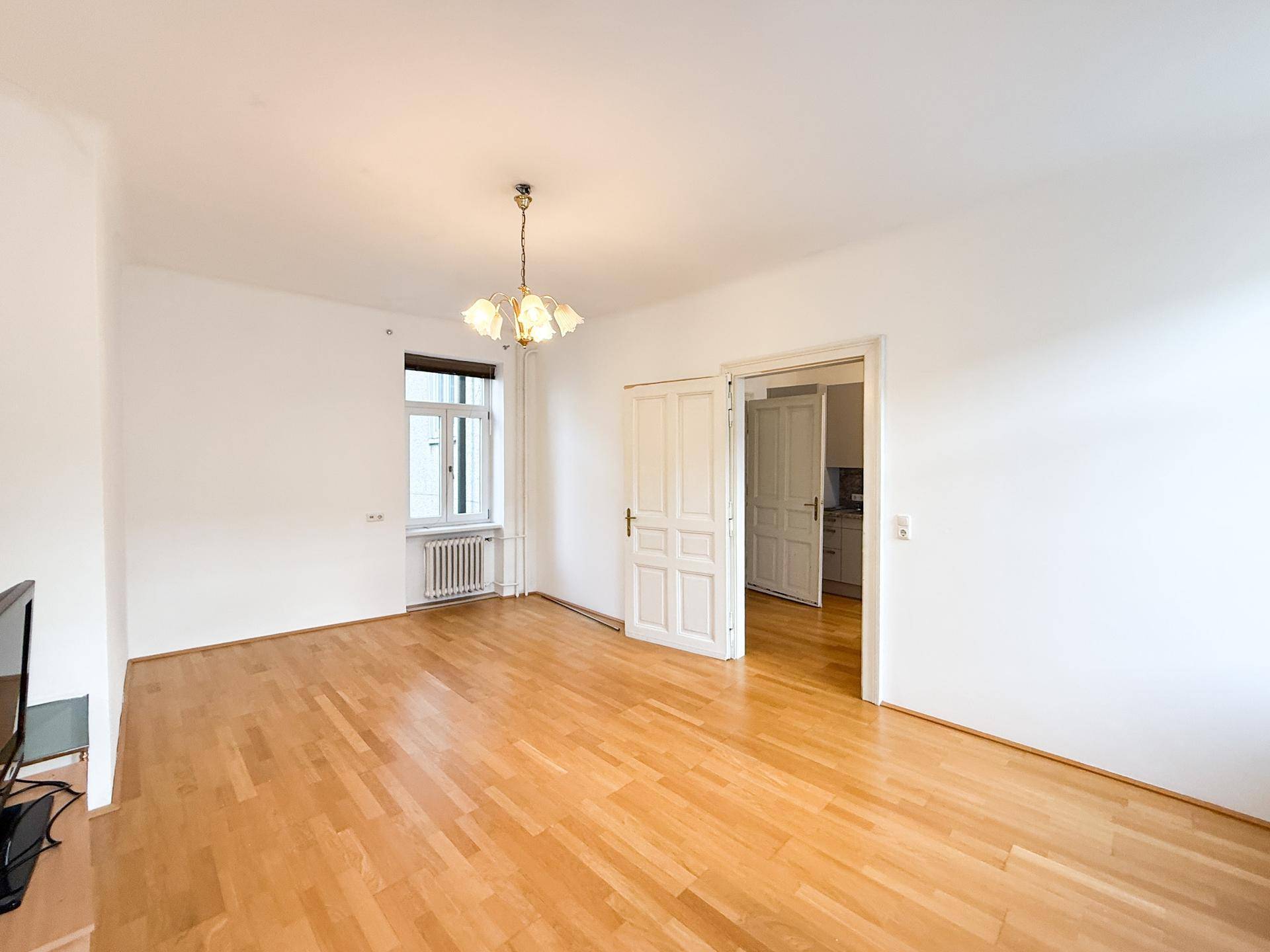 Helles Wohnzimmer mit Holzboden und Zugang zu einem weiteren Raum.