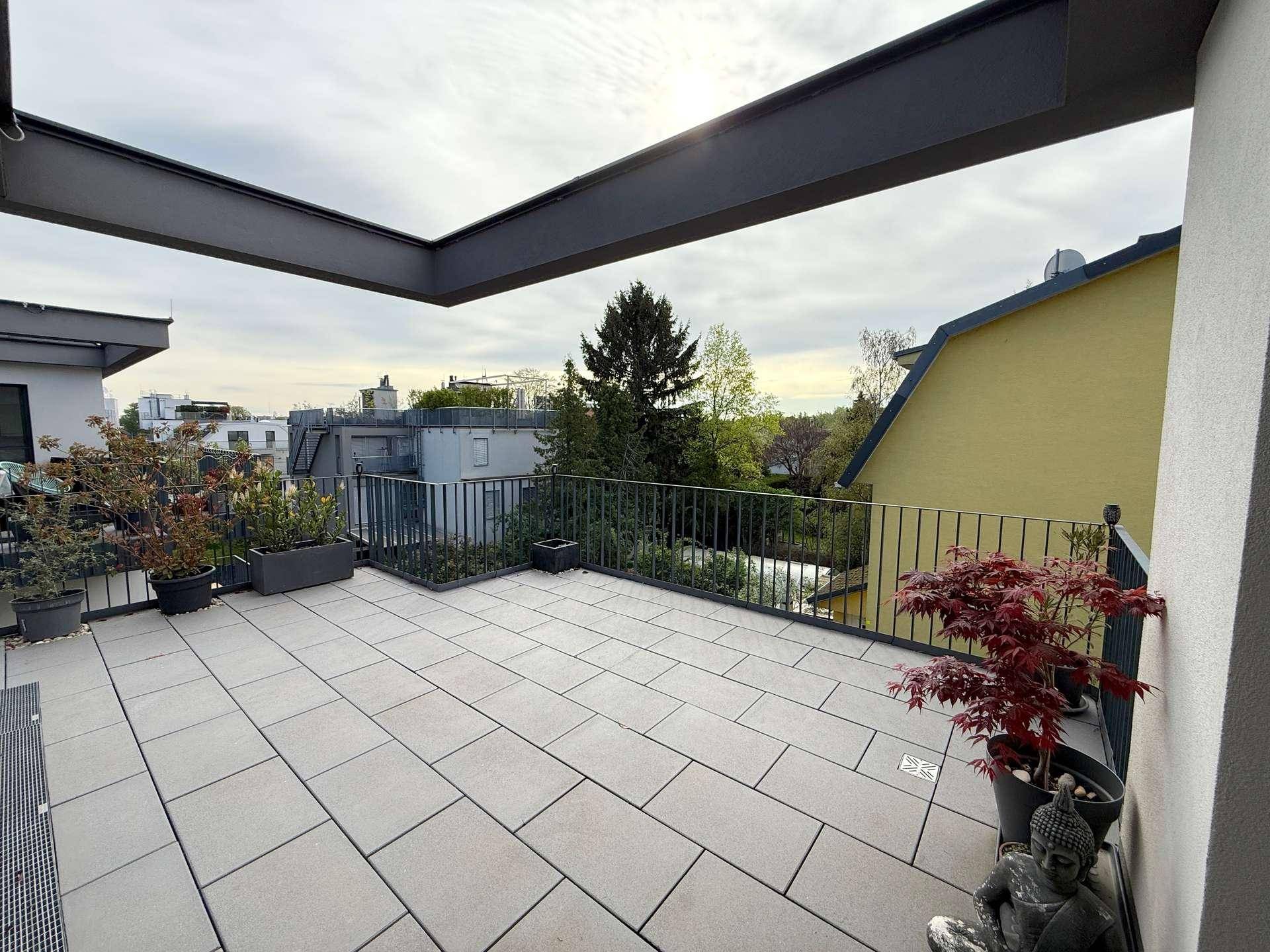 Geräumige Dachterrasse mit Fliesenboden und Metallgeländer, umgeben von Topfpflanzen.