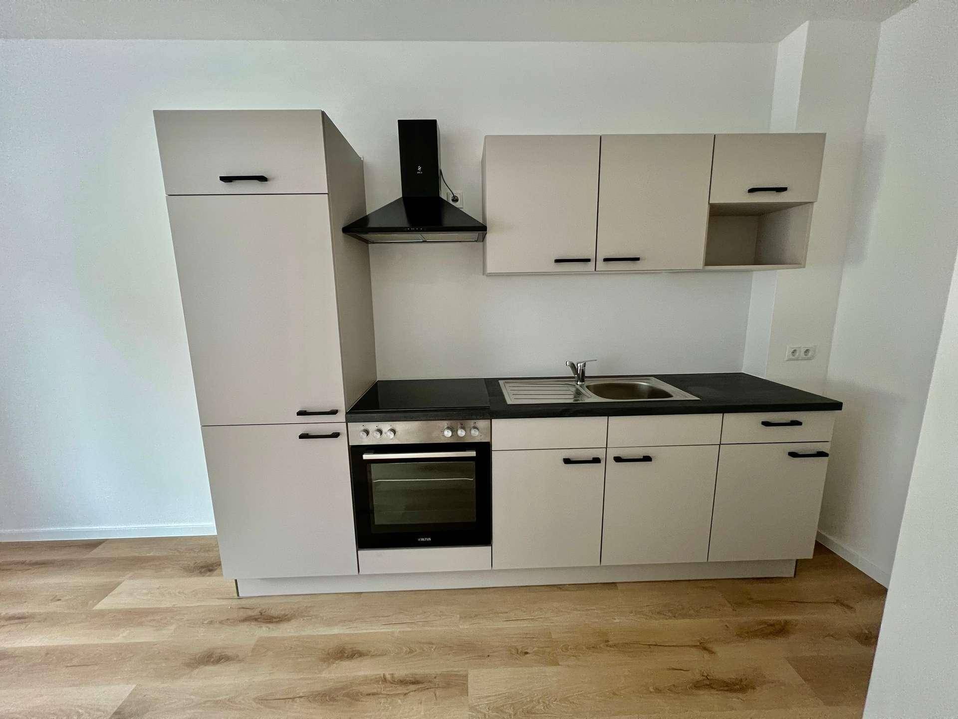 Moderne Küchenzeile mit hellen Schränken, dunkler Arbeitsplatte und integriertem Backofen.
