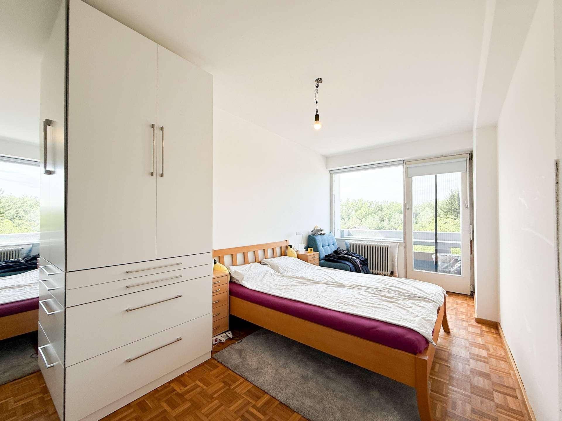 Schlafzimmer mit Holzbett, großem Kleiderschrank und Zugang zum Balkon.