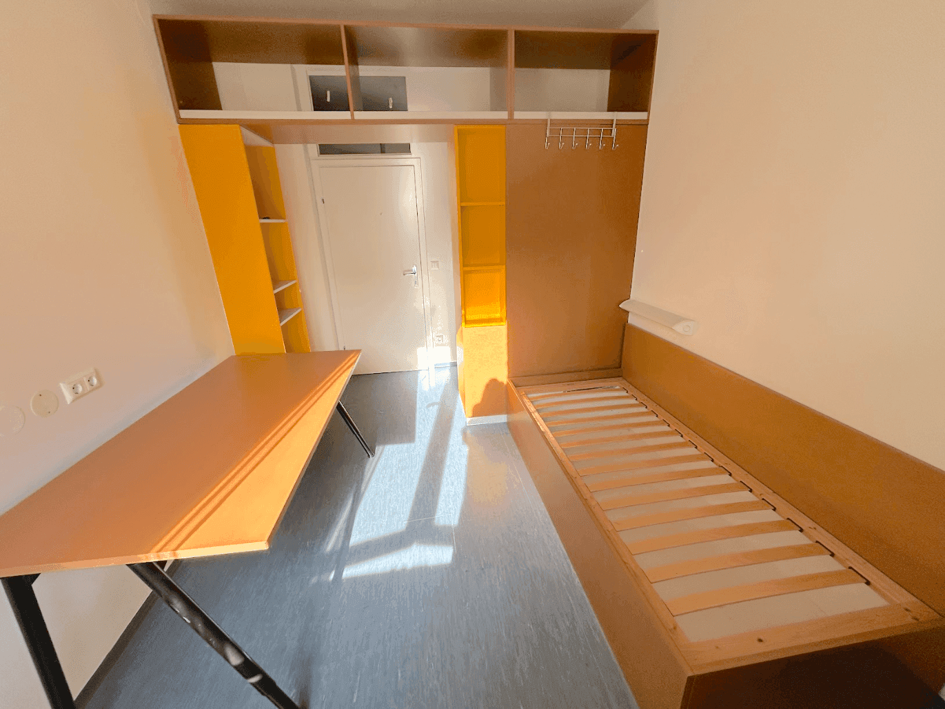 Sonnenlichtdurchflutetes Schlafzimmer mit Bettrahmen, Schreibtisch und gelben Möbeln.
