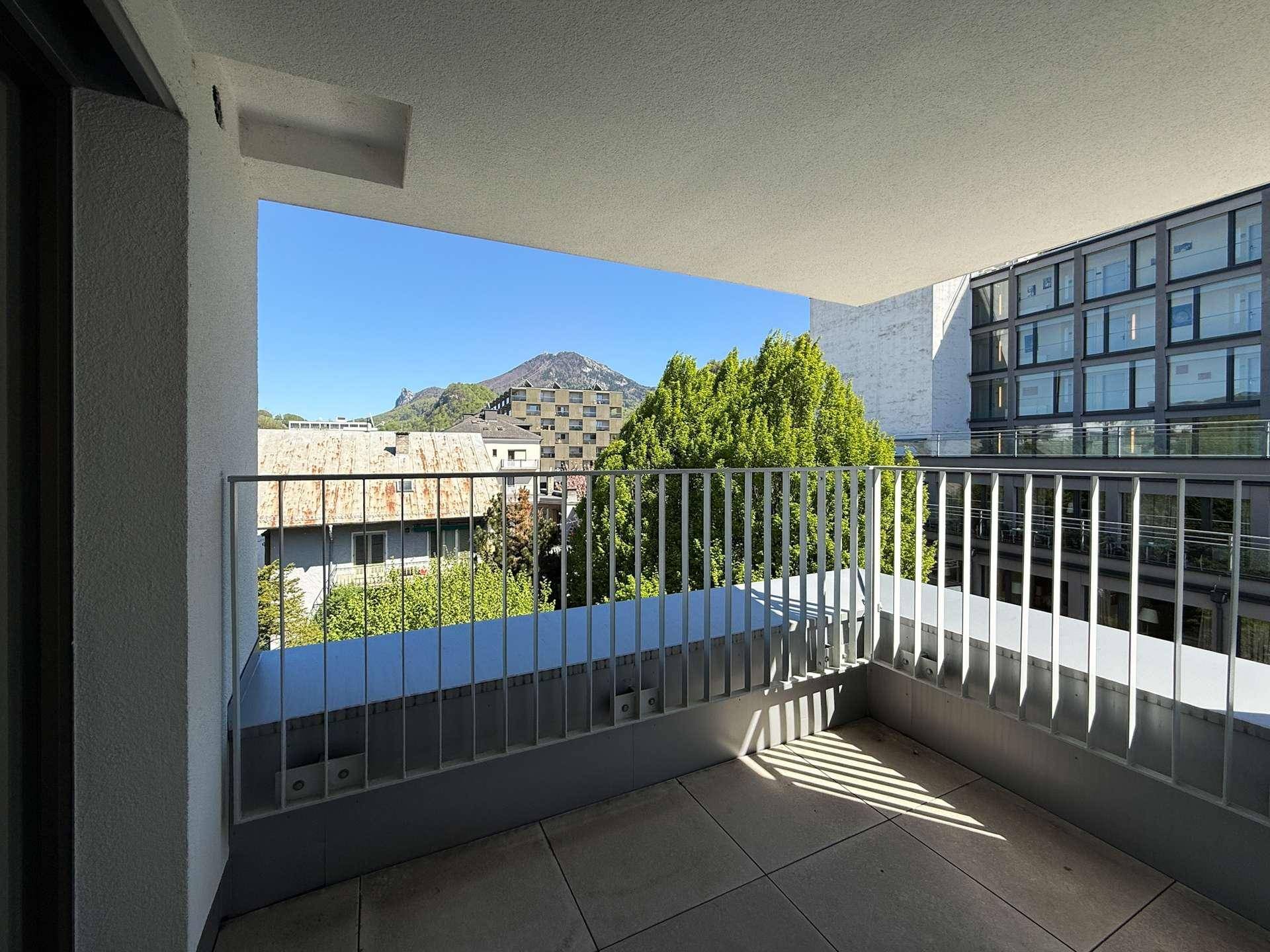 Heller Balkon mit Fliesenboden, Metallgeländer und Bergblick in der Ferne.