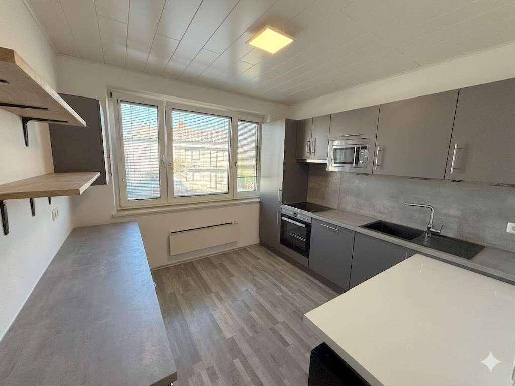 Moderne Küche mit grauen Schränken, integrierten Geräten und einem Fenster.