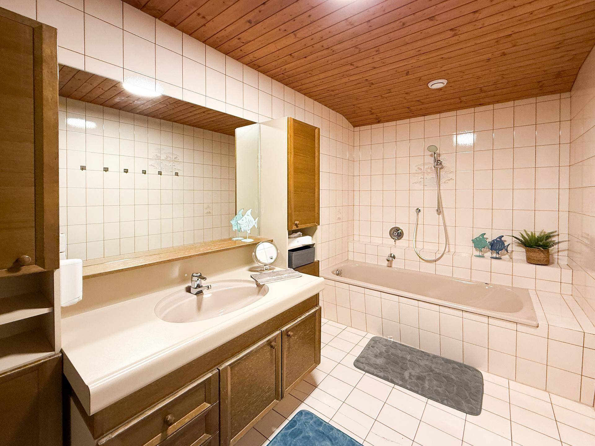 Geräumiges Badezimmer mit Badewanne, Waschtisch und Fliesen an Wänden und Decke.