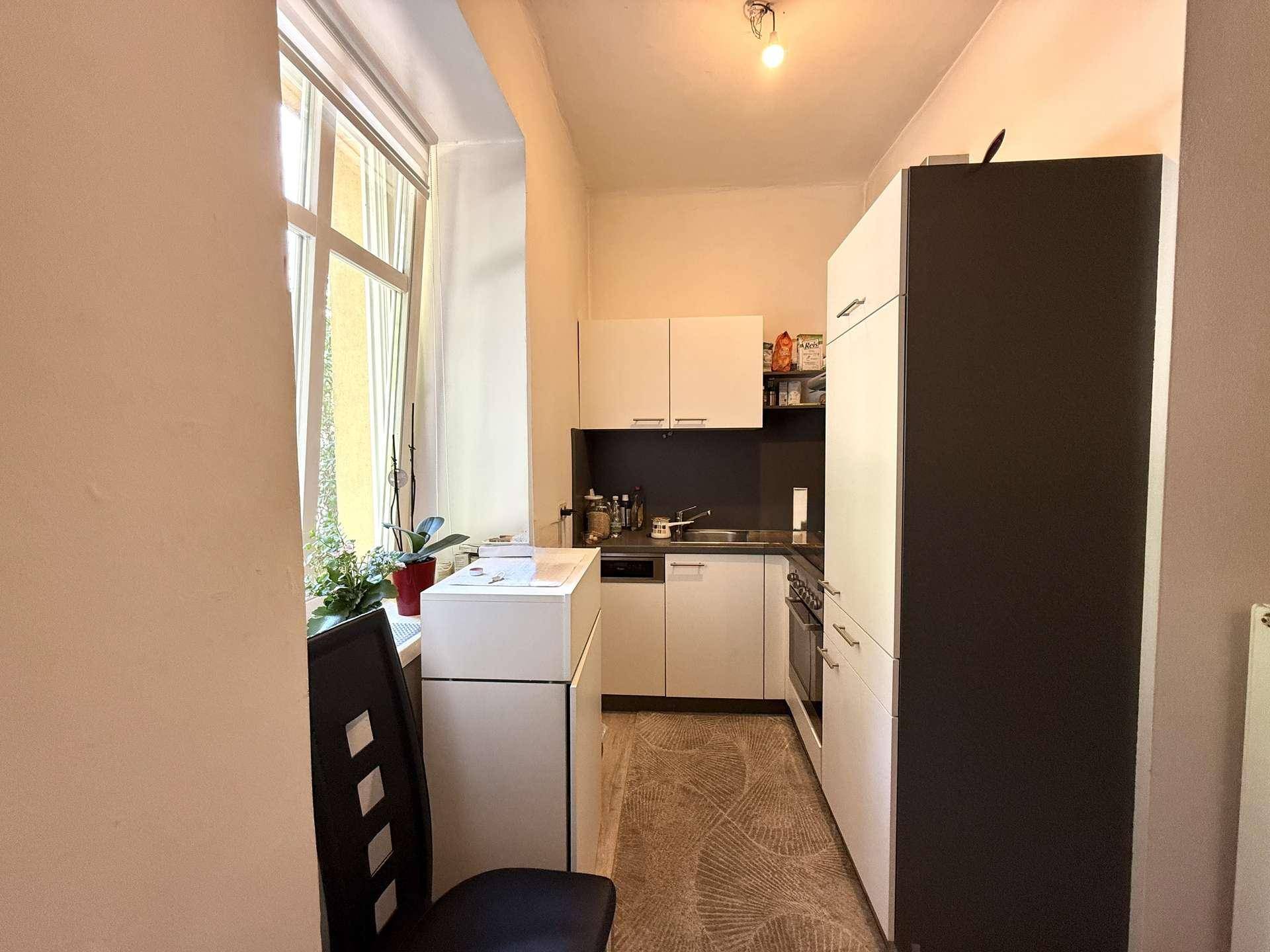 Kleine, funktionale Küche mit weißen Schränken, dunkler Arbeitsplatte und Fenster.