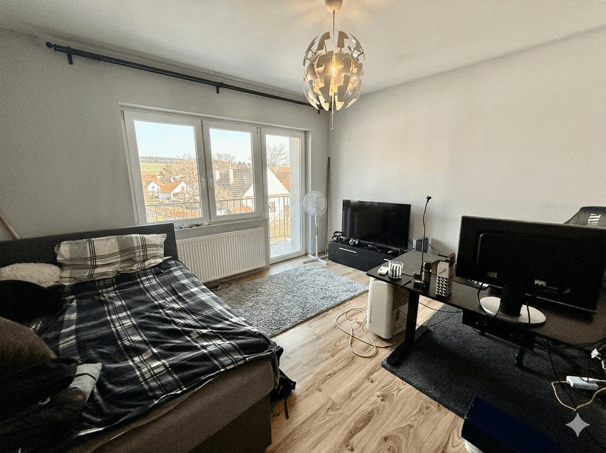 Schlafzimmer mit Holzboden, Schreibtisch und Zugang zu einem kleinen Balkon mit Aussicht.