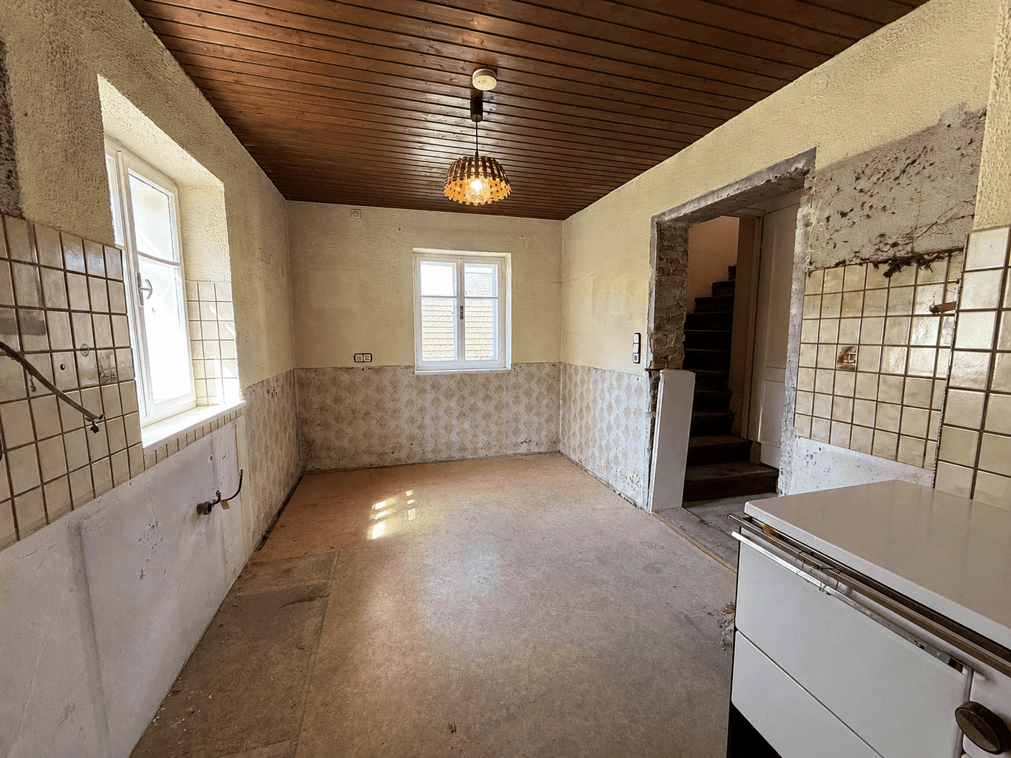 Alte Küche im Renovierungszustand mit Holzdecke, Fliesen und einem traditionellen Ofen.