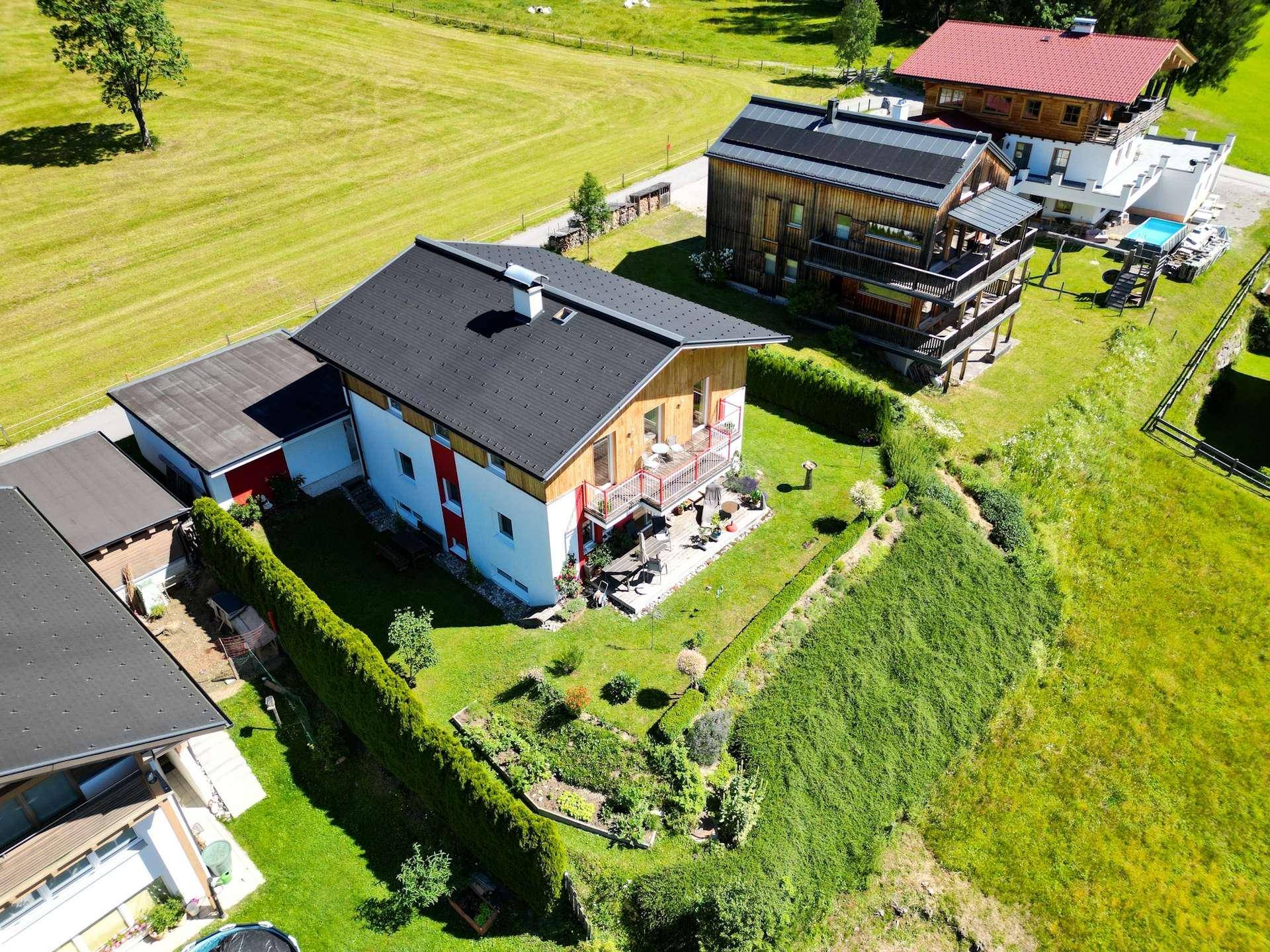 Vogelperspektive des Anwesens mit gepflegtem Garten, umgeben von üppiger Natur und Bergpanorama.