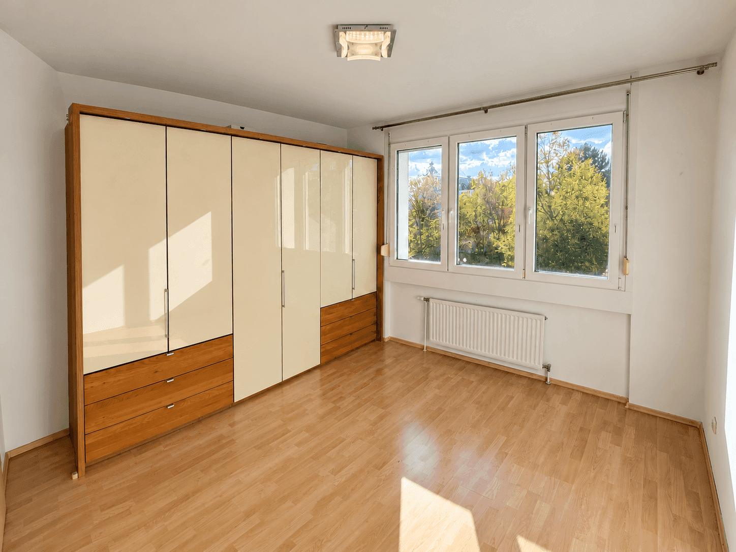 Helles Schlafzimmer mit Laminatboden, großem Einbauschrank und Fenstern mit Blick ins Grüne.