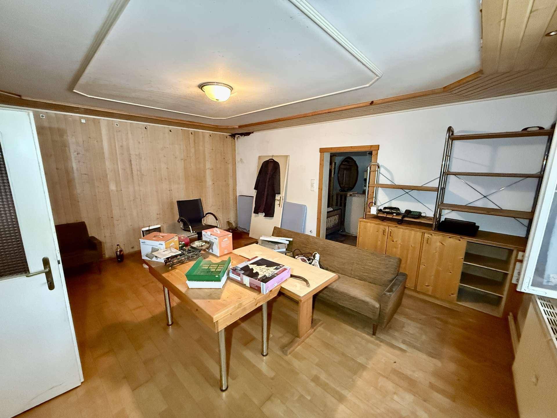 Wohnraum mit Holzboden, teilweise Holzverkleidung und einfacher Einrichtung, die Gemütlichkeit ausstrahlt.